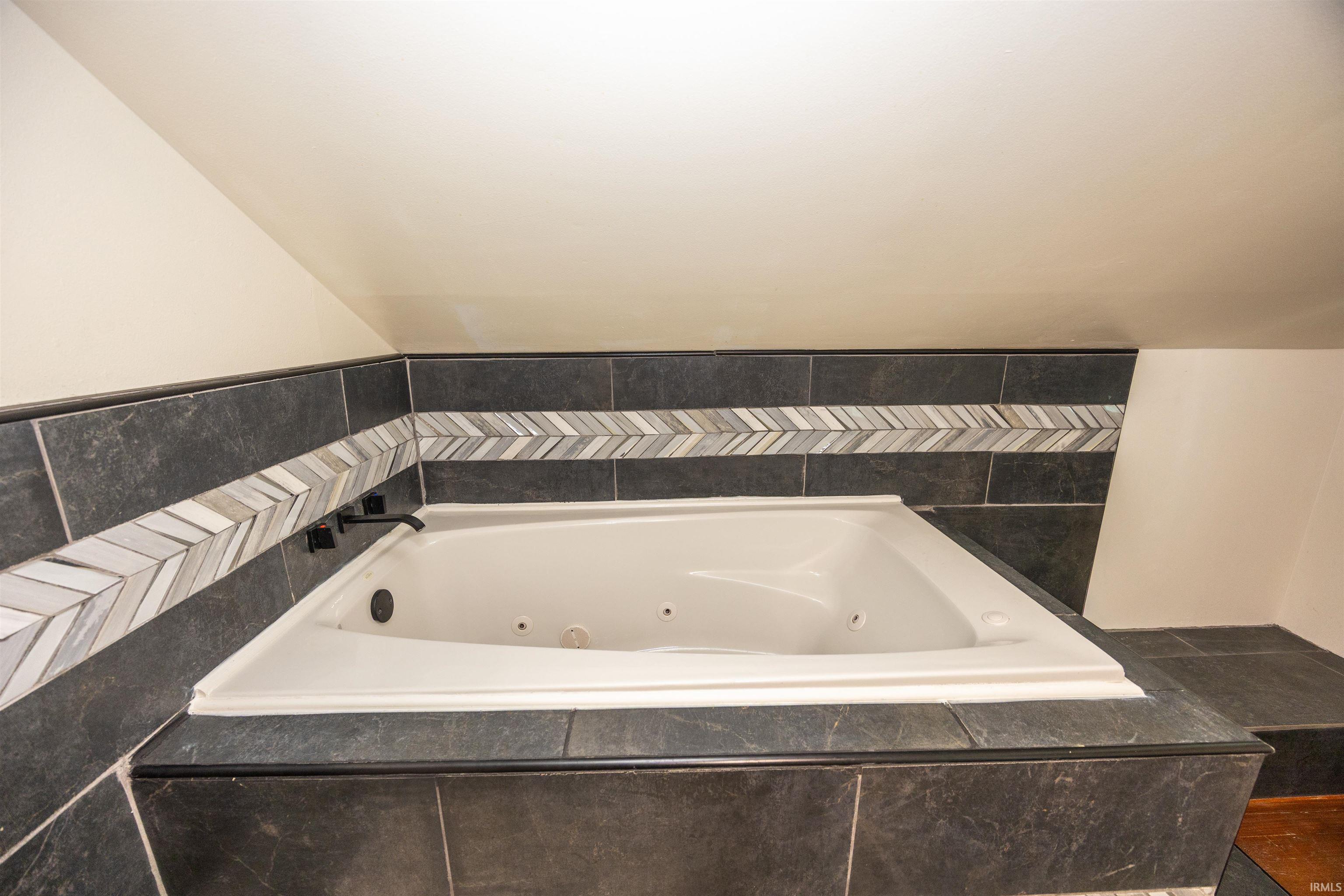 Corner jetted tub set within a dark tile surround, featuring a chevron-patterned accent band
