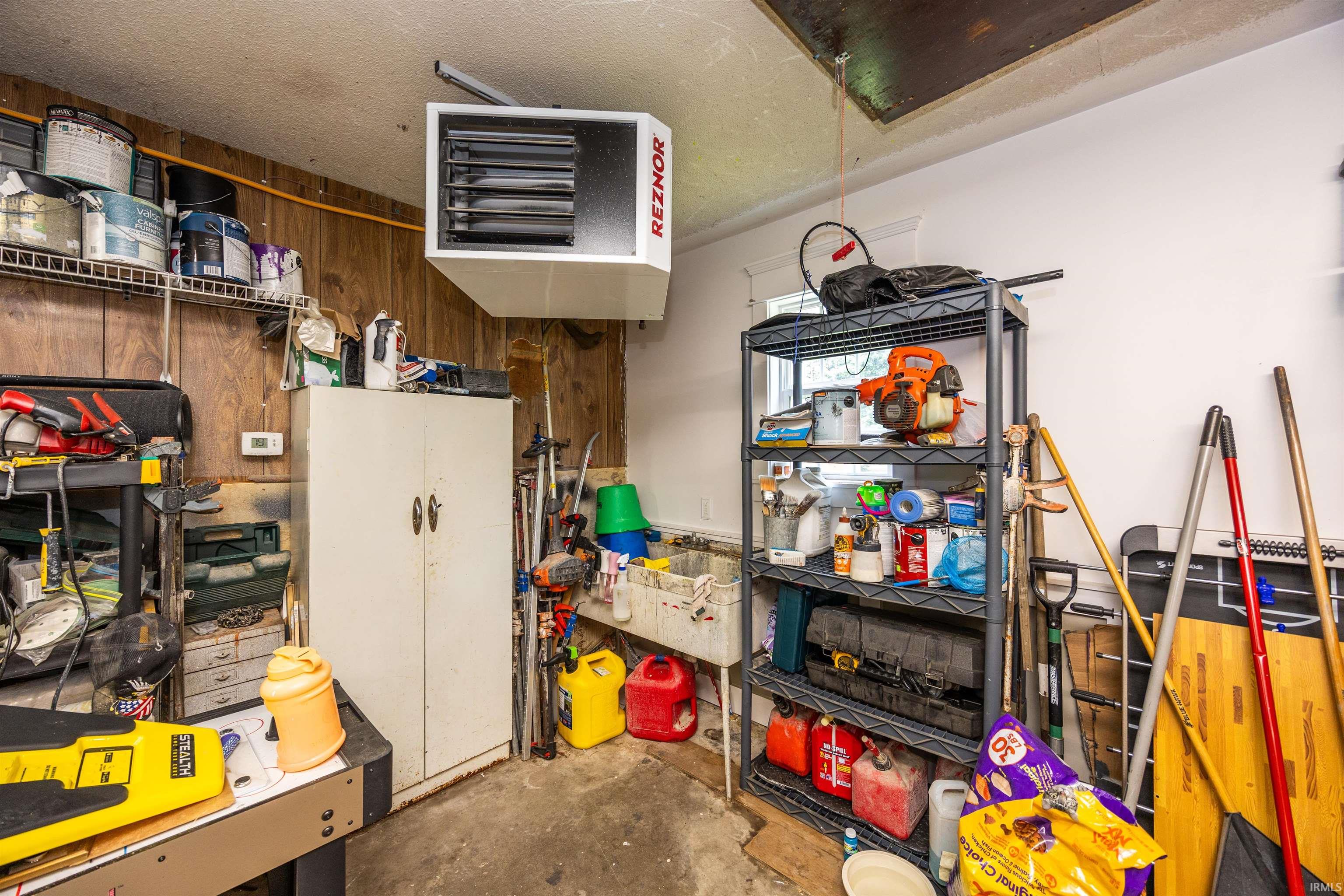Utility room featuring a ceiling-mounted Reznor heater, concrete flooring, and wall-mounted shelving