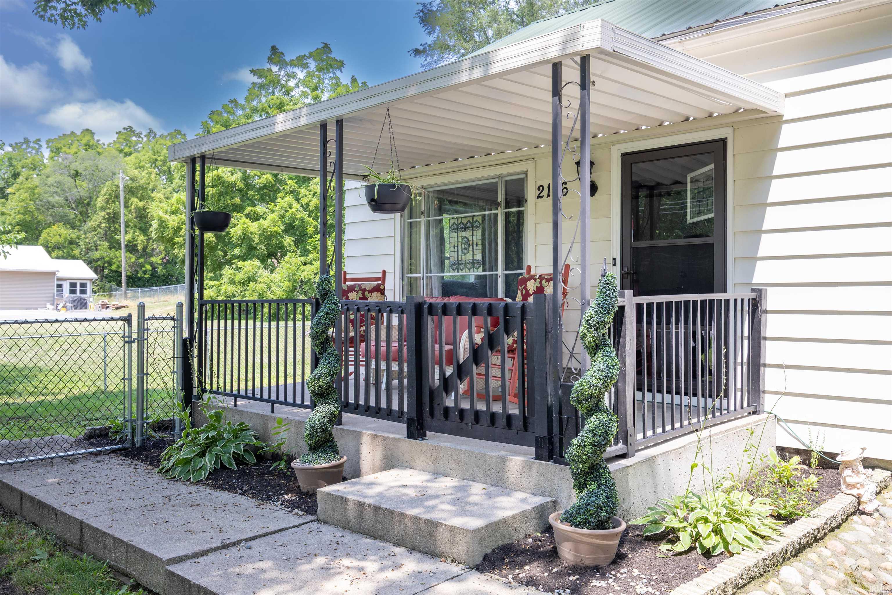 Covered front porch featuring black wrought iron railings, a black screen door, white siding, and concrete steps