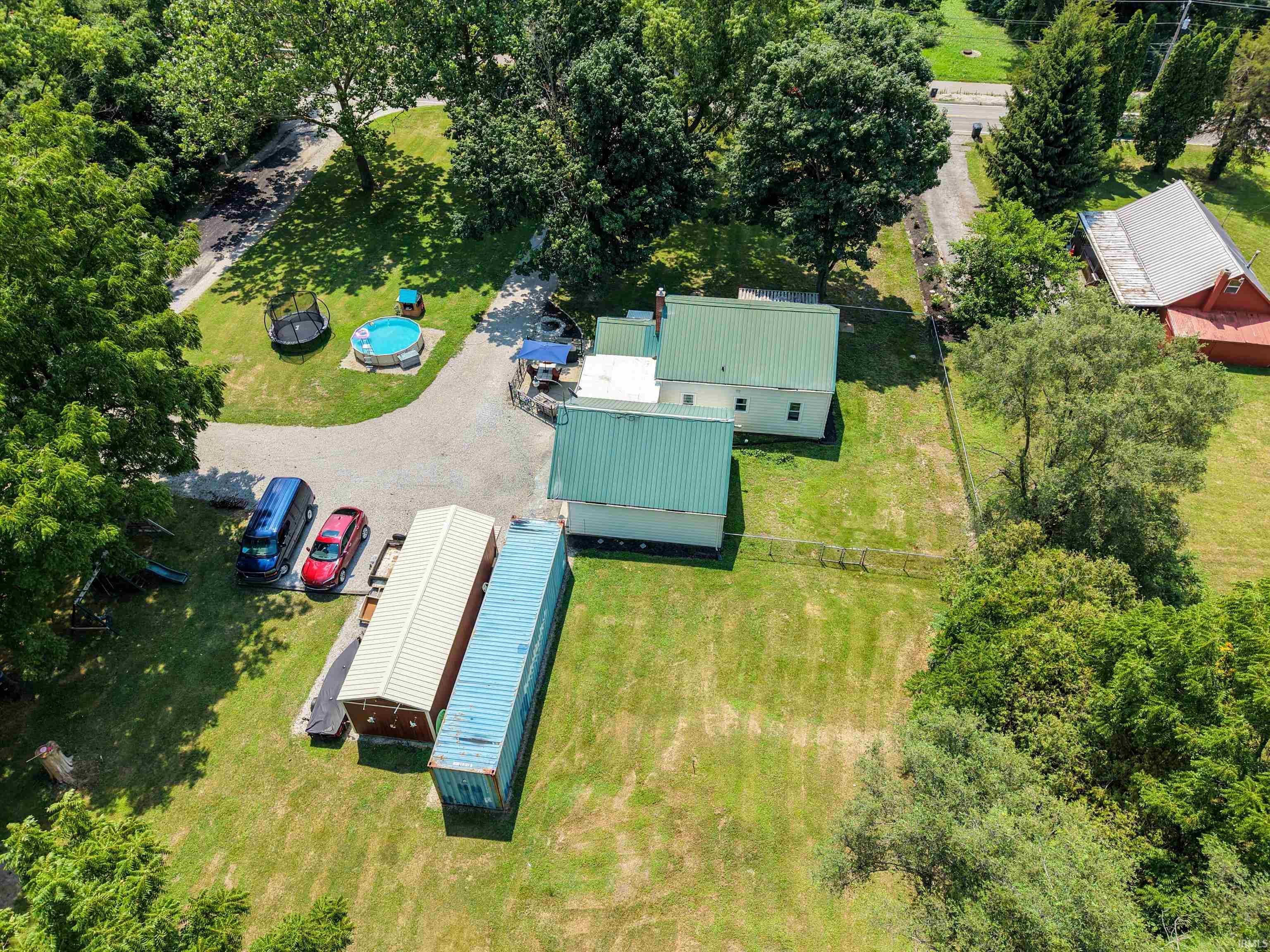 Expansive property featuring a main residence with a green metal roof, an additional outbuilding with a matching green metal roof, a gravel driveway, and a large grassy yard with mature trees