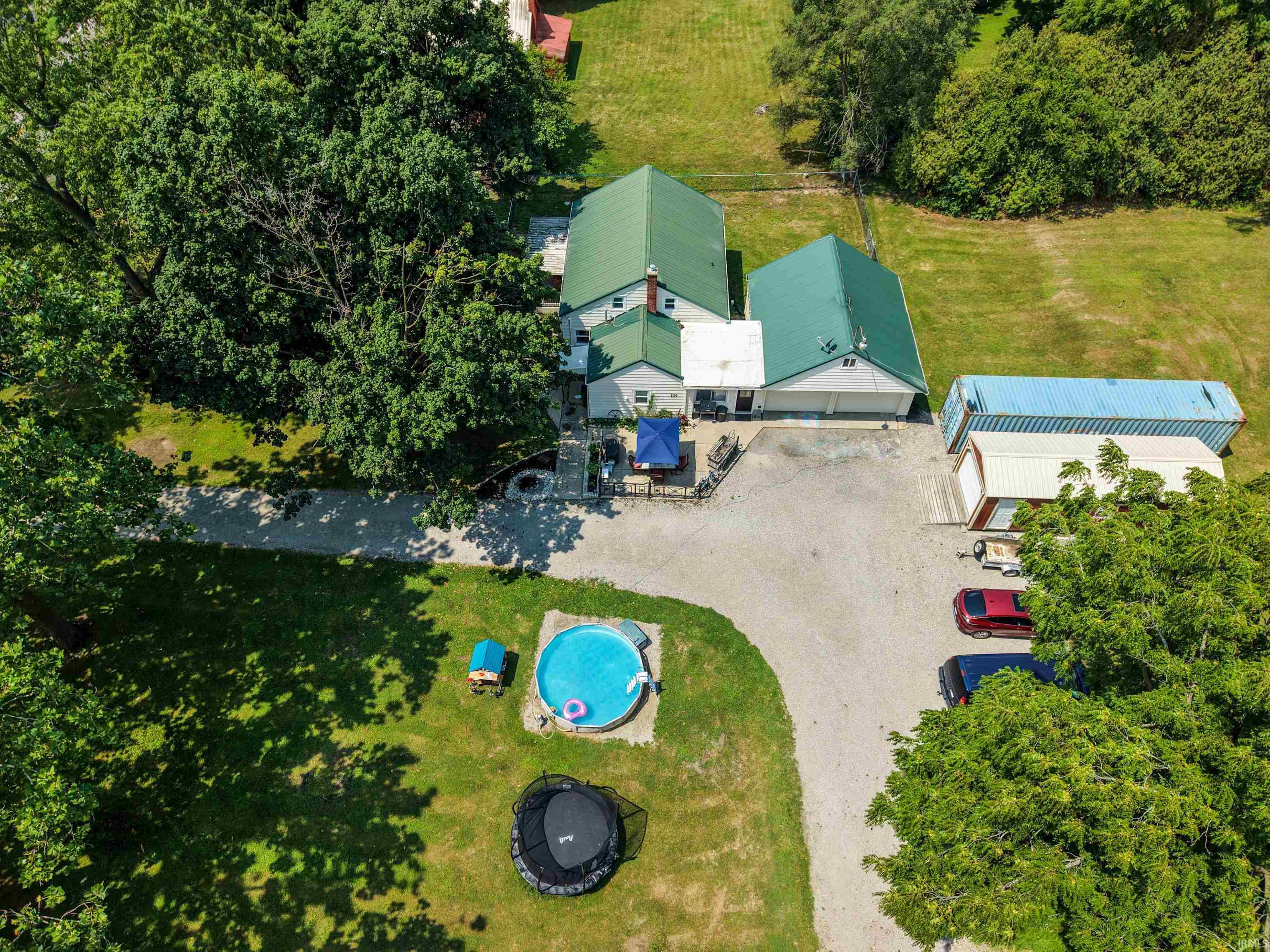 Expansive property featuring a residence with a green metal roof, a large detached garage, a gravel parking area, and additional outbuildings