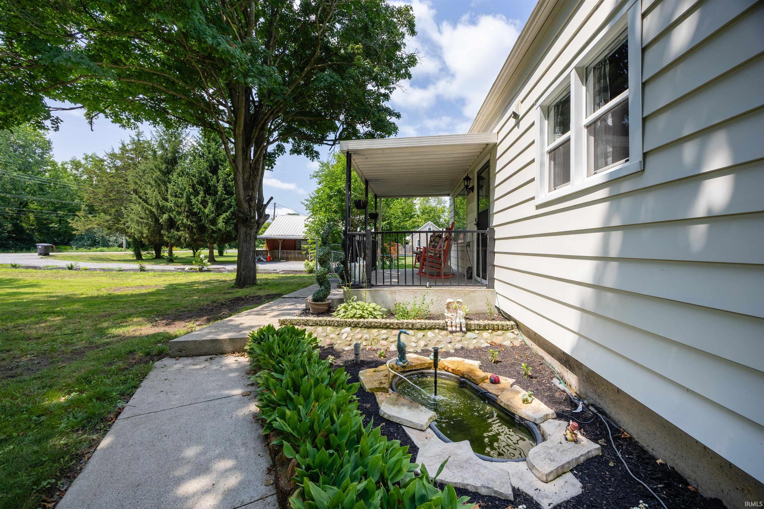 Covered front porch with black railings, a landscaped garden bed featuring a water feature, and a concrete walkway