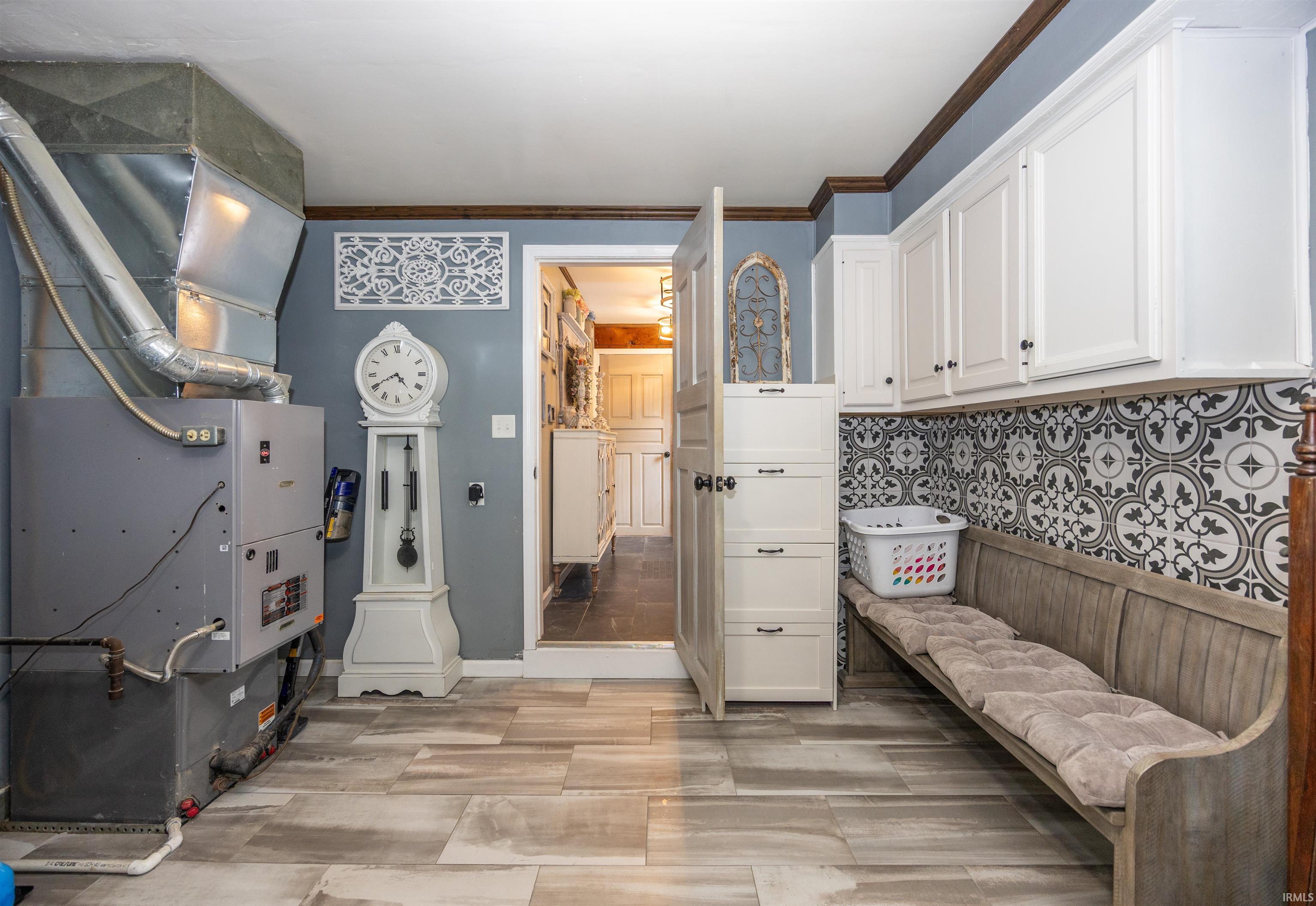 Utility space featuring wood-finish flooring, white cabinetry, decorative tile backsplash, and a built-in bench with cushioned seating