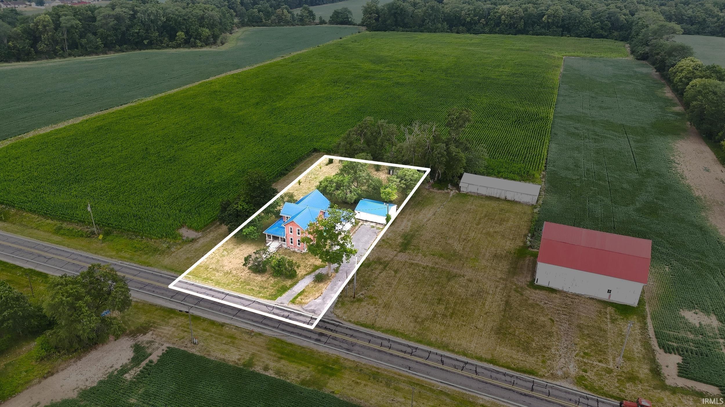 Aerial overview showcasing a property with a vibrant blue roof and pink exterior, a detached garage, and a red-roofed barn structure