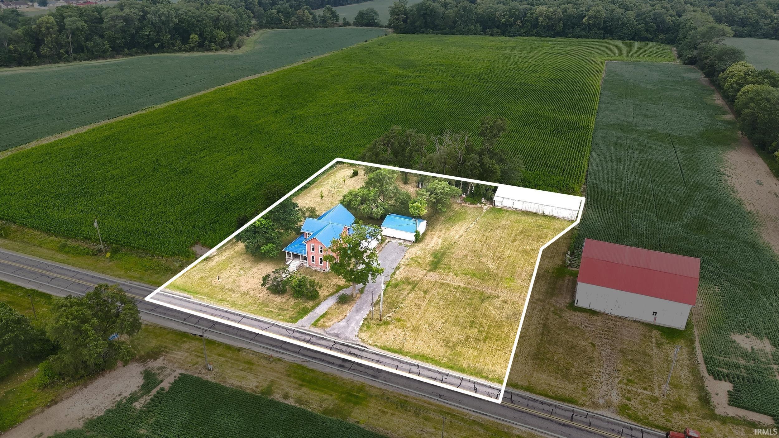 Property featuring a two-story residence with a blue roof, an auxiliary structure with a blue roof, and an additional white-roofed outbuilding, all situated on a parcel with a paved driveway