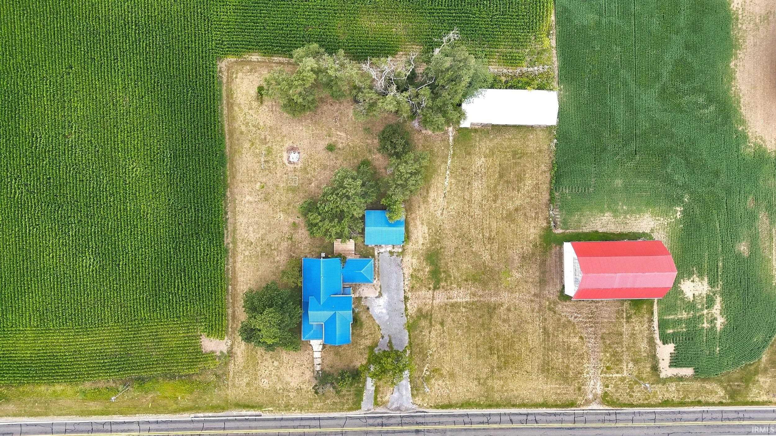 Agricultural property with three structures featuring blue and red roofs, surrounded by expansive cultivated fields
