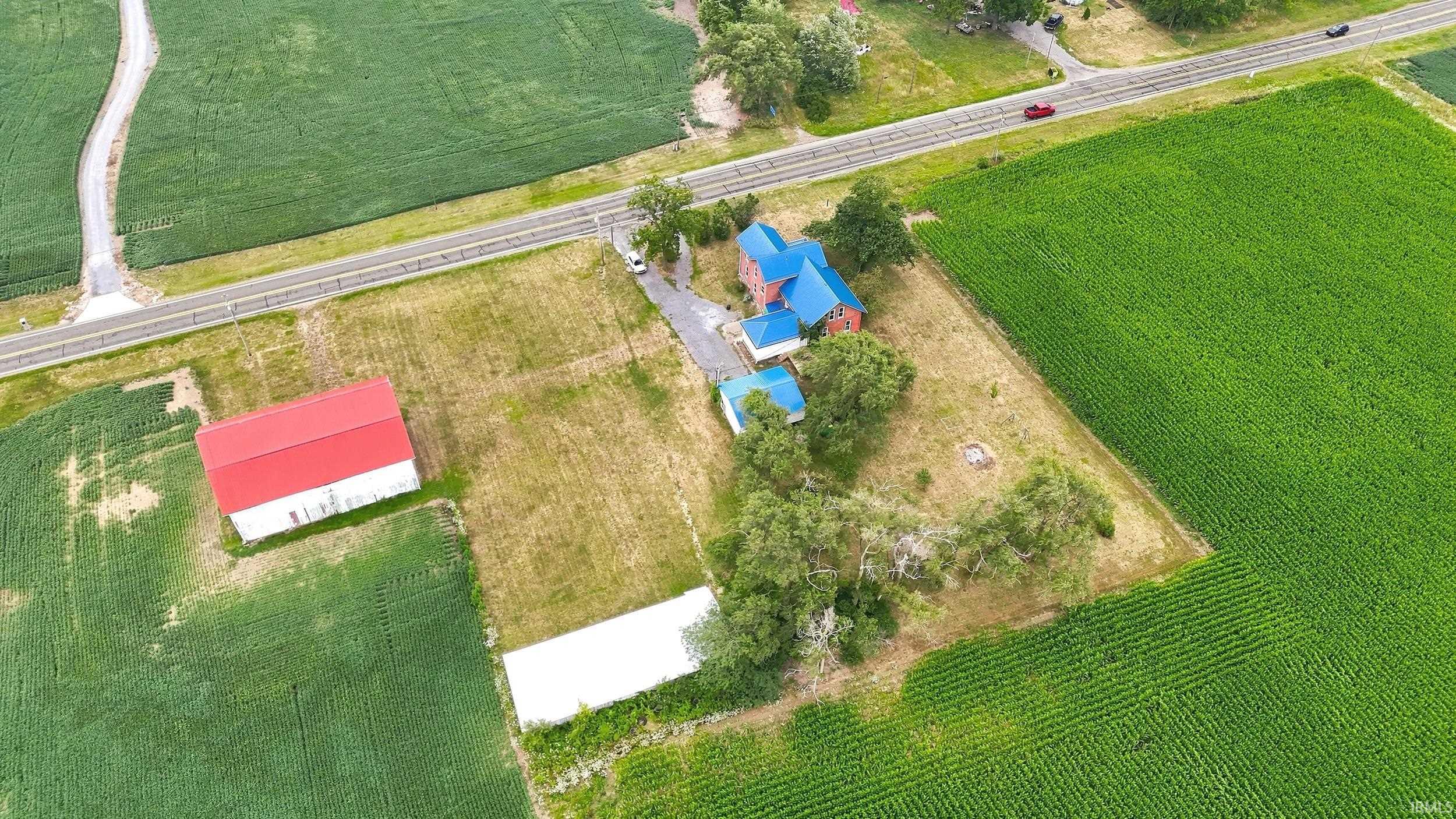 Aerial perspective showcasing a property featuring a main residence with a blue roof, multiple outbuildings, and a large white barn with a red roof