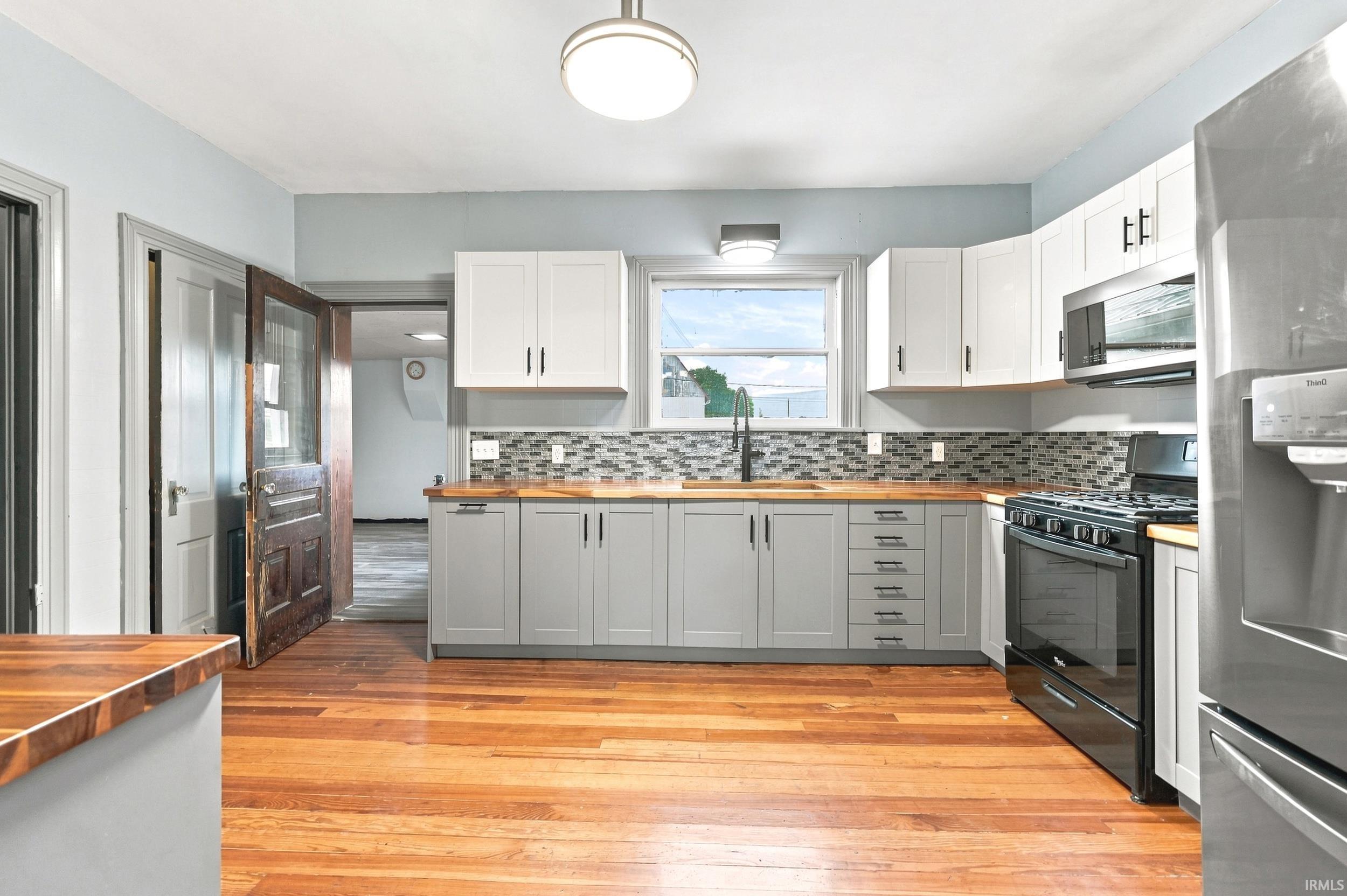 Kitchen featuring wood-finish flooring, two-tone cabinetry with white upper and gray lower cabinets, and wood countertops