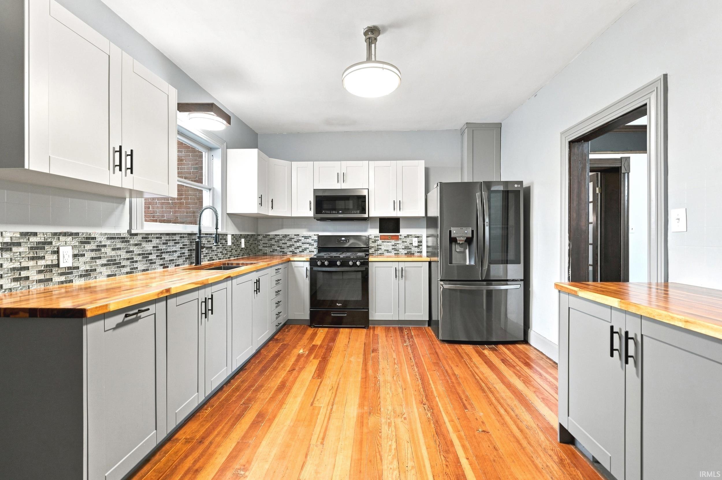 Kitchen with wood-finish flooring, two-tone cabinetry, and wood countertops