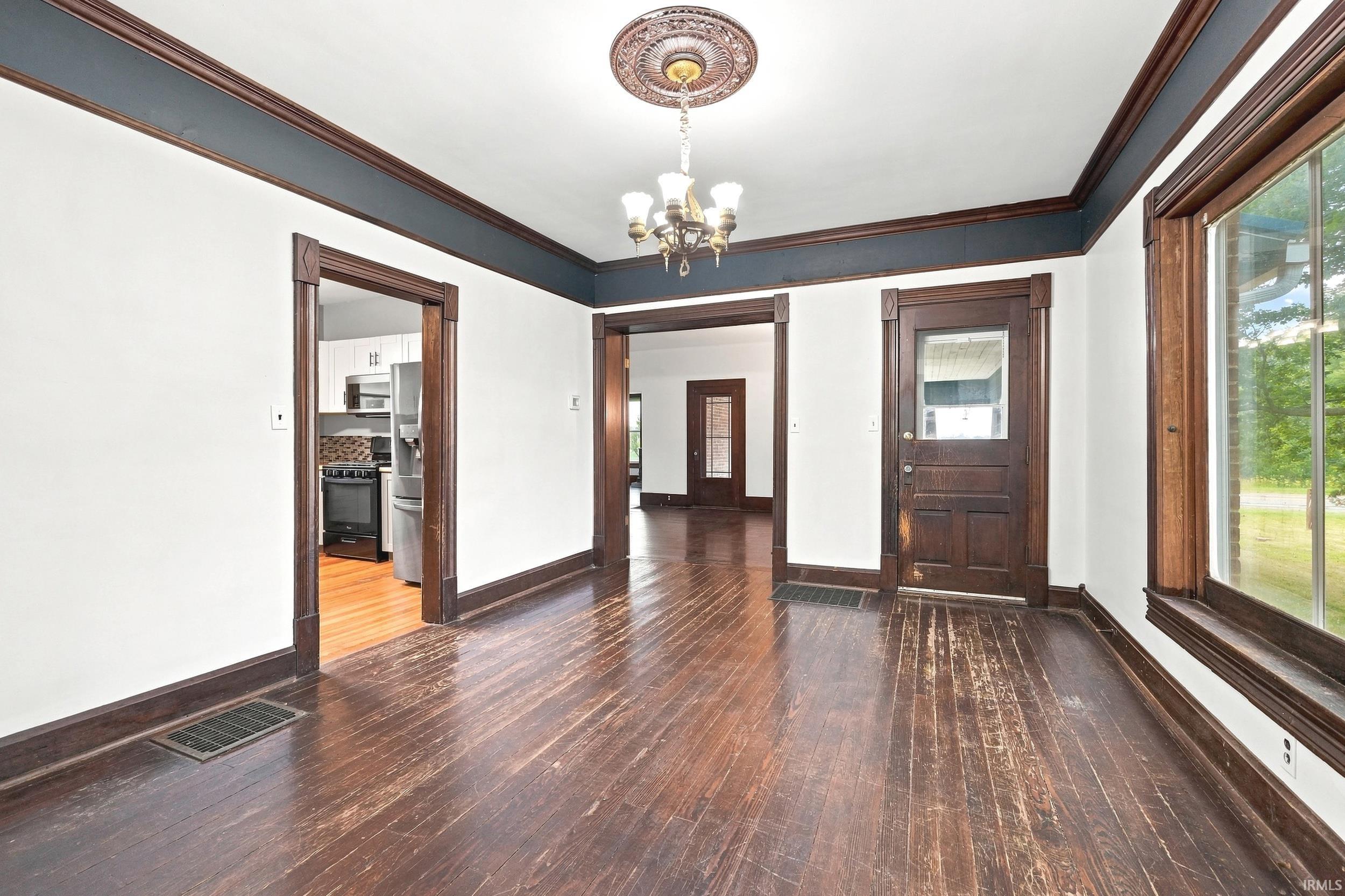 Spacious interior featuring dark wood-finish flooring, white walls with a contrasting dark accent band, and an ornate ceiling medallion with a chandelier