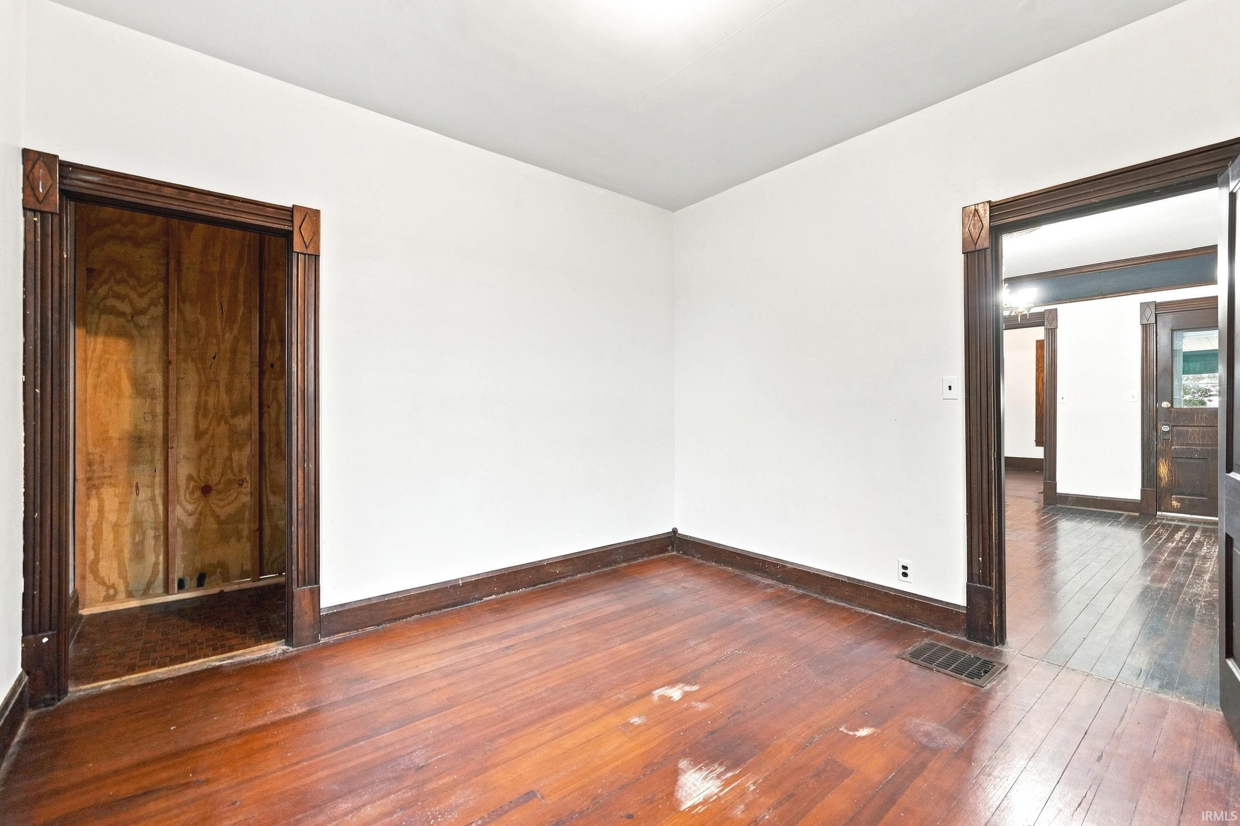 Interior room featuring rich wood-finish flooring, white walls, and dark wood trim