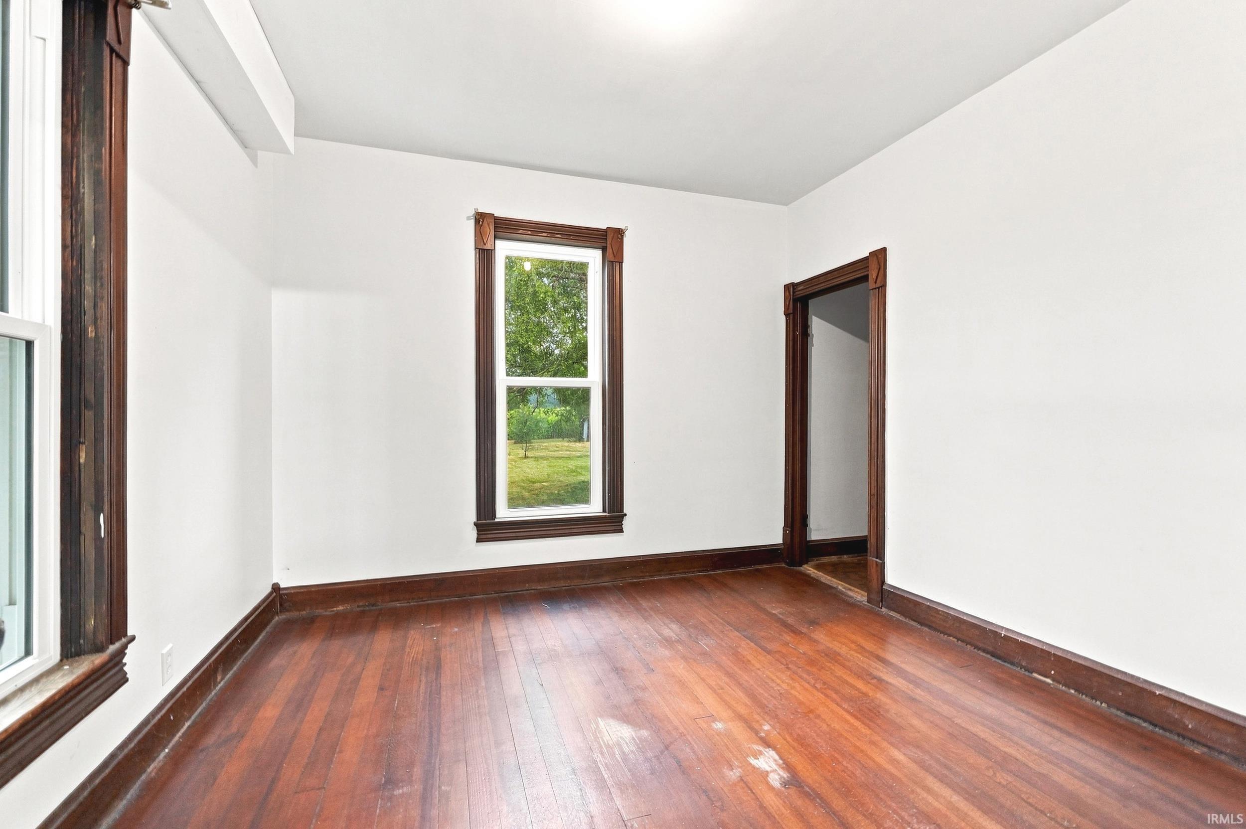 Interior space featuring wood-finish flooring, white painted walls, and dark wood trim around windows and doorways