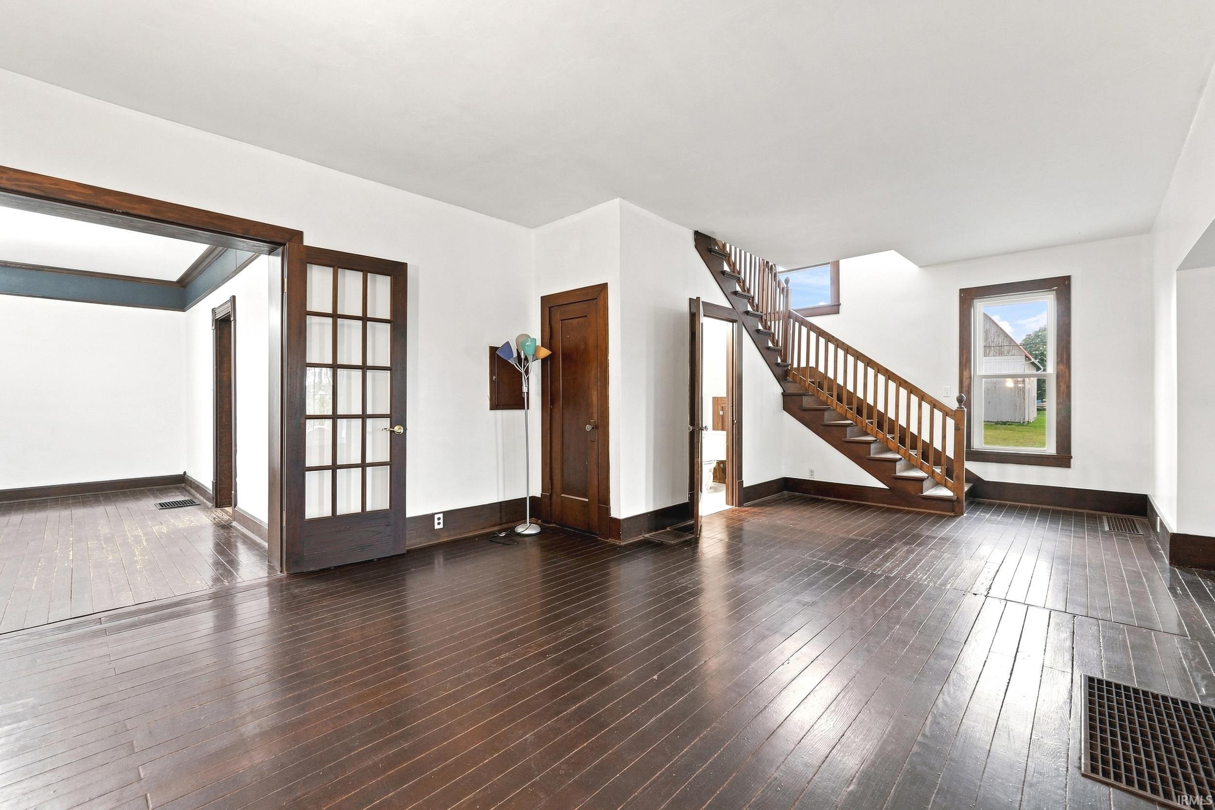 Spacious interior featuring dark wood-finish flooring, a traditional wooden staircase with balusters, and white walls