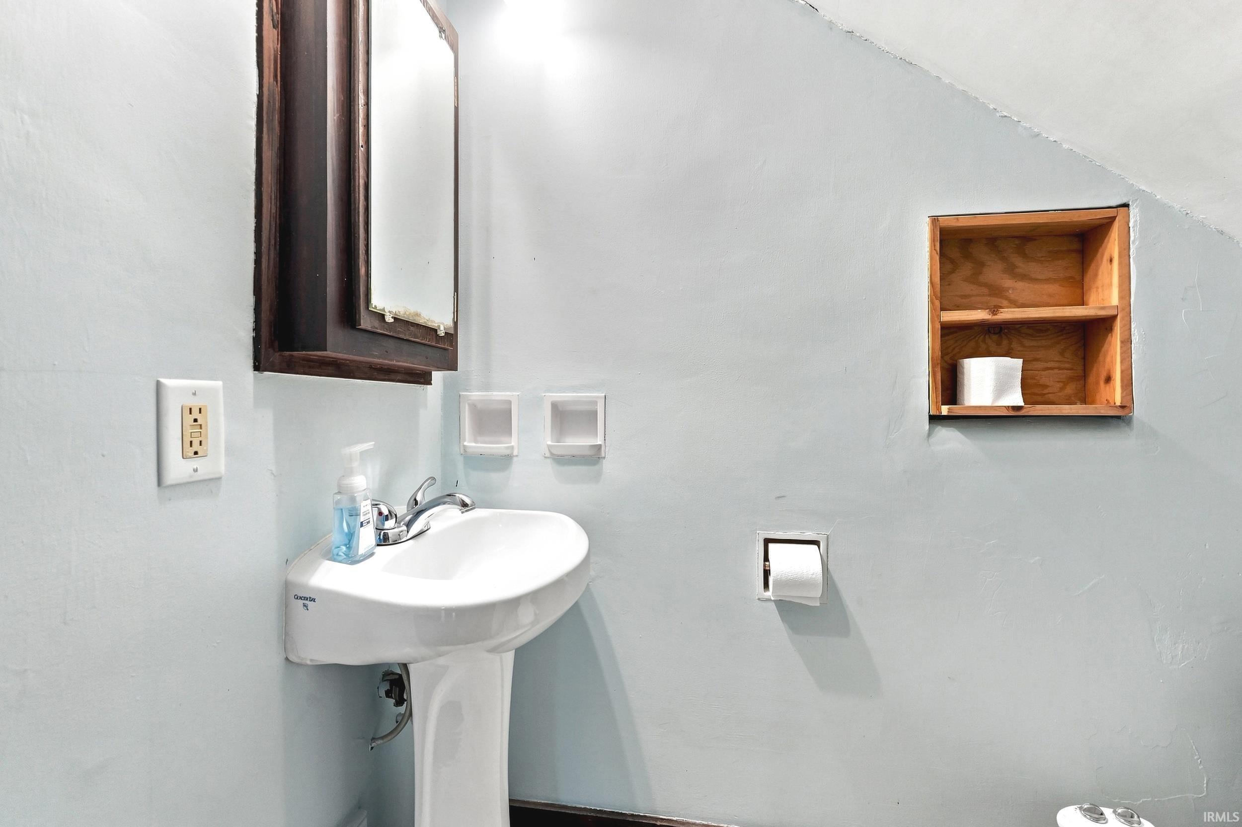 Pedestal sink with chrome faucet, framed mirror, and built-in wood shelving