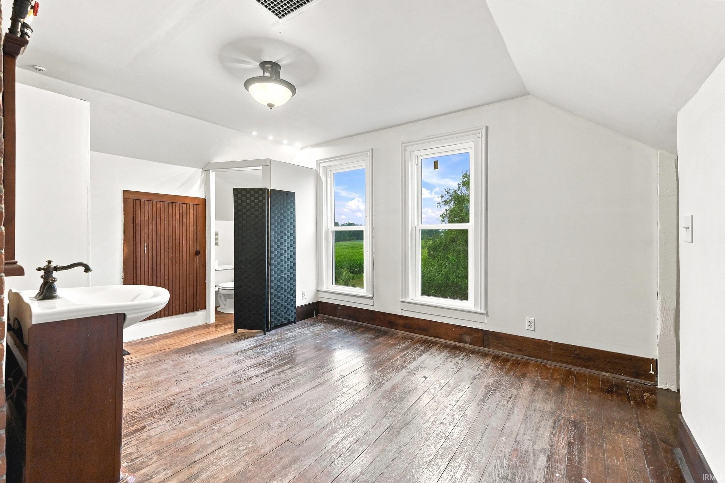 Room featuring two prominent windows, sloped ceilings, and wood-finish flooring