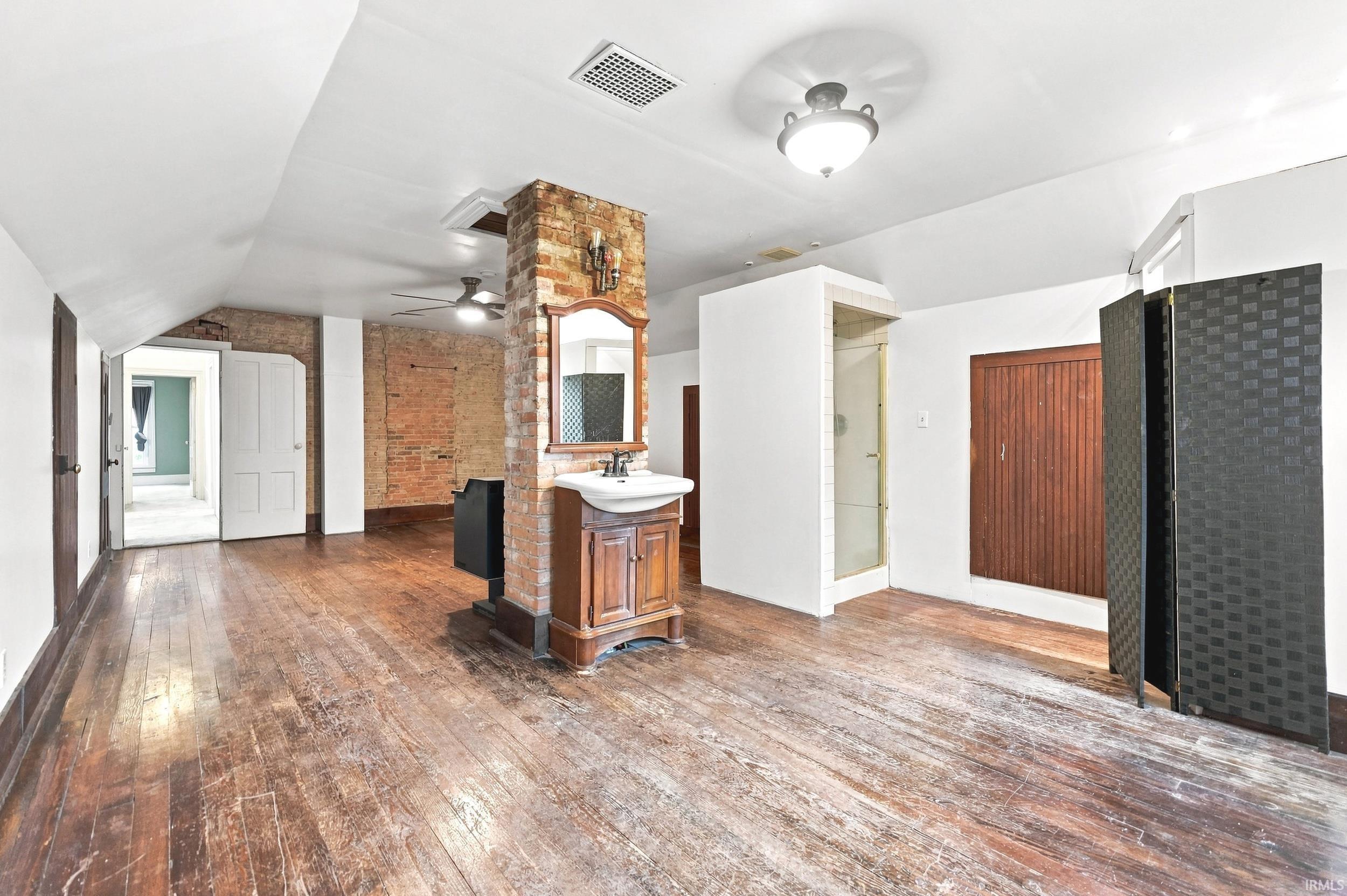 Spacious upper-level room featuring distressed wood-finish flooring, exposed brick accents, an integrated vanity with basin sink, and a glass-enclosed shower