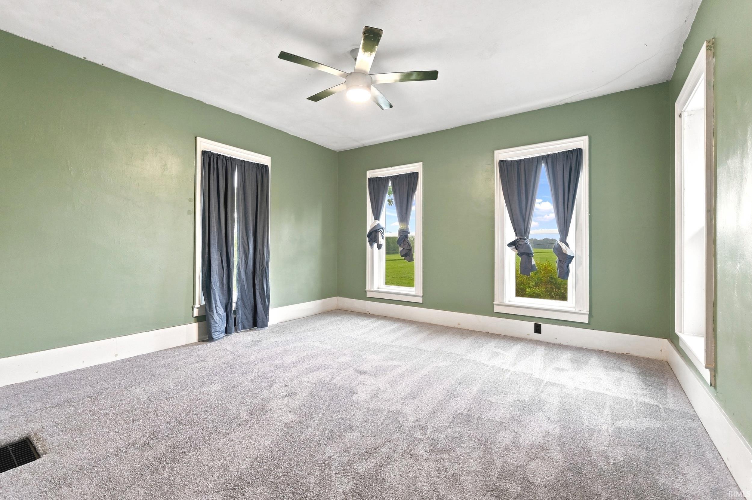 Spacious room featuring light green walls, a ceiling fan with integrated lighting, and gray carpet flooring