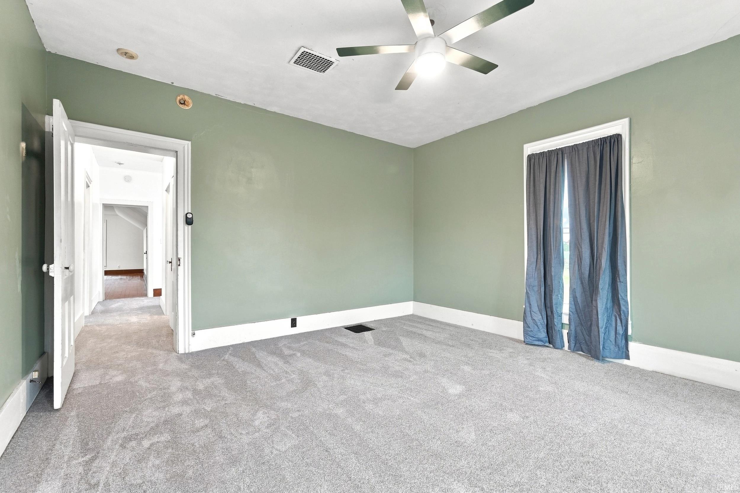 Carpeted room featuring a ceiling fan with integrated lighting, a window with curtains, and a doorway leading to an interior hallway