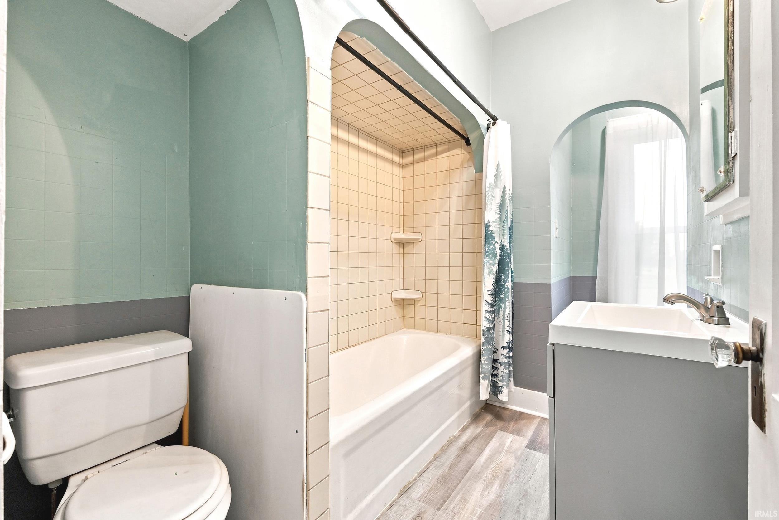 Bathroom featuring a full tub with tiled surround, a white toilet, and a vanity with a white basin