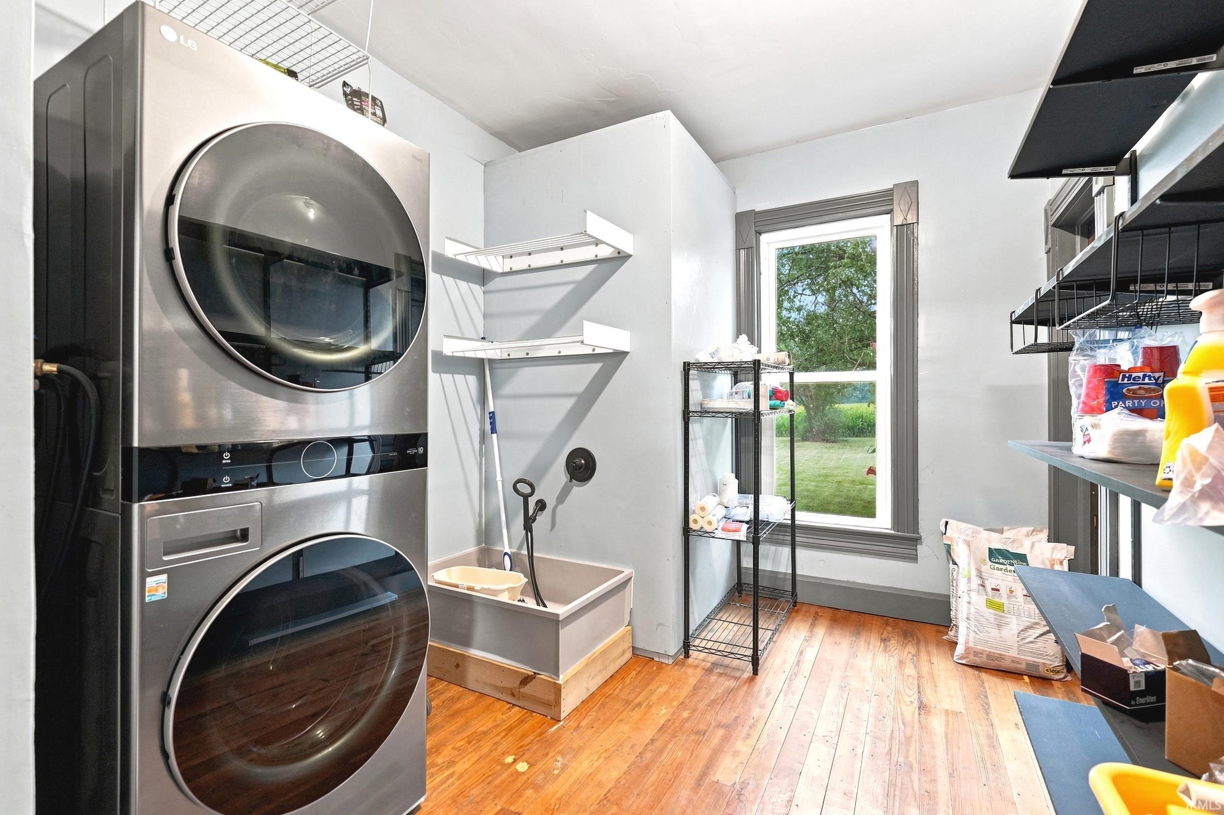 Dedicated laundry area featuring stacked appliances, a utility sink, a window with trim, and wood-finish flooring