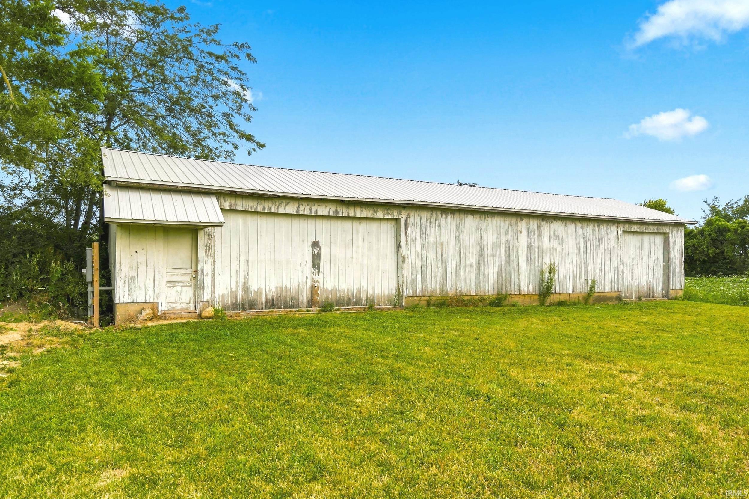 White-sided barn structure with a metal roof and multiple large entryways