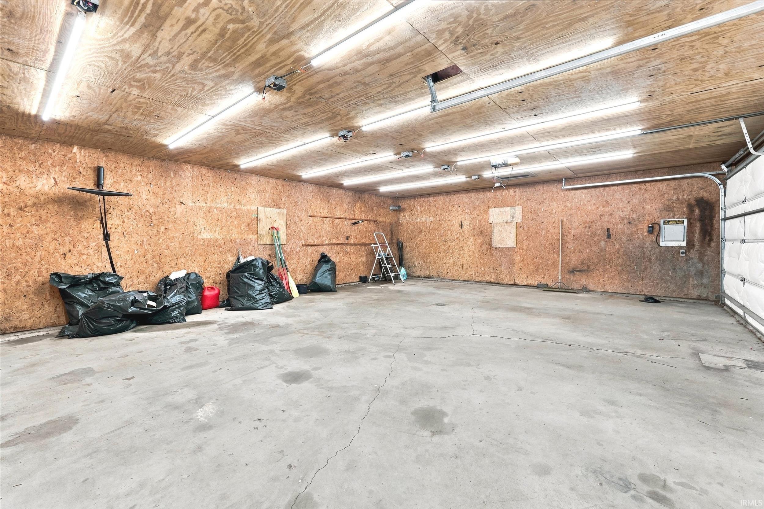 Spacious garage with concrete flooring, wood-finish walls and ceiling, multiple overhead fluorescent light fixtures, and a white paneled garage door