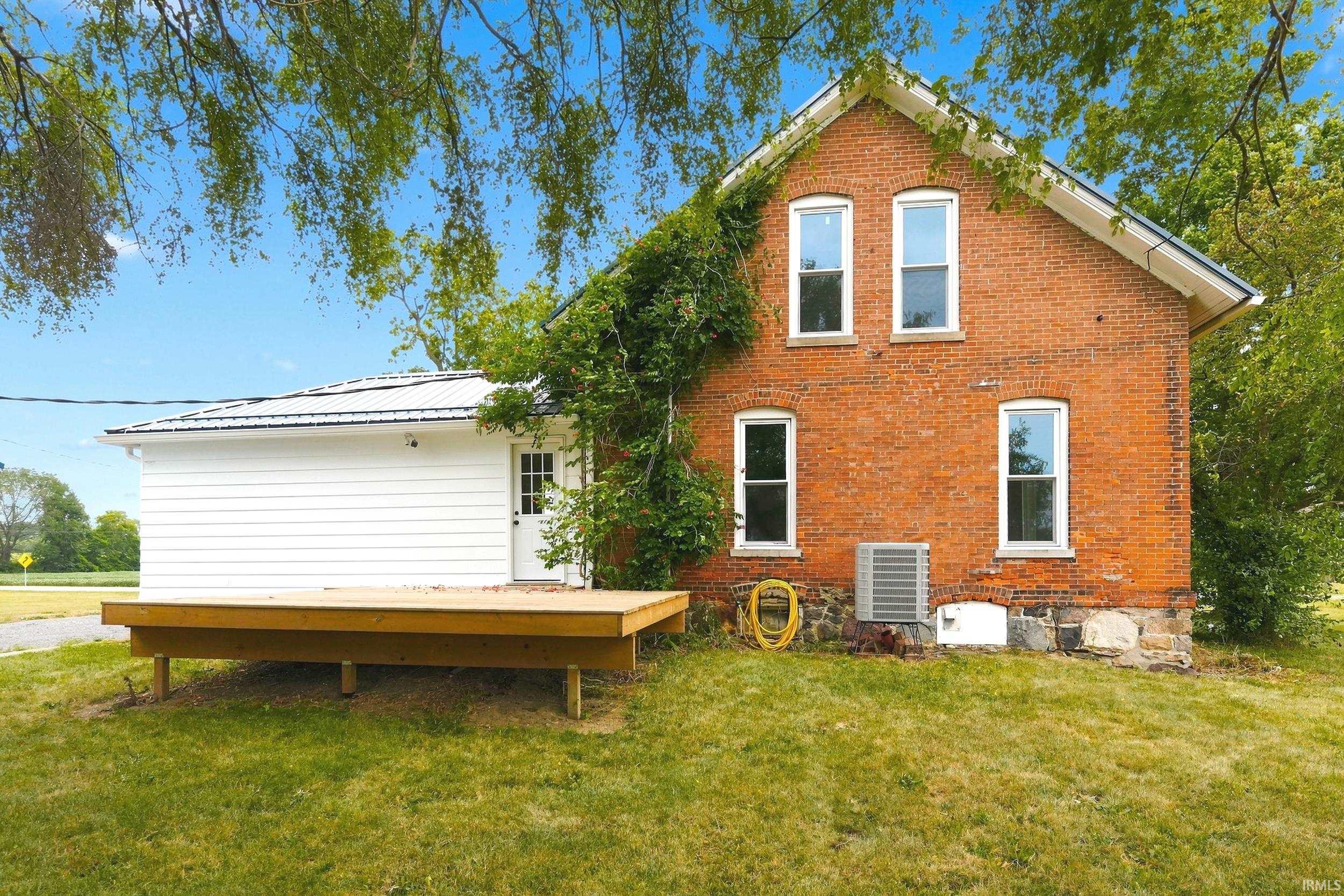 Brick exterior with white window frames, a newly constructed wood deck, and an attached extension featuring white horizontal siding and a metal roof