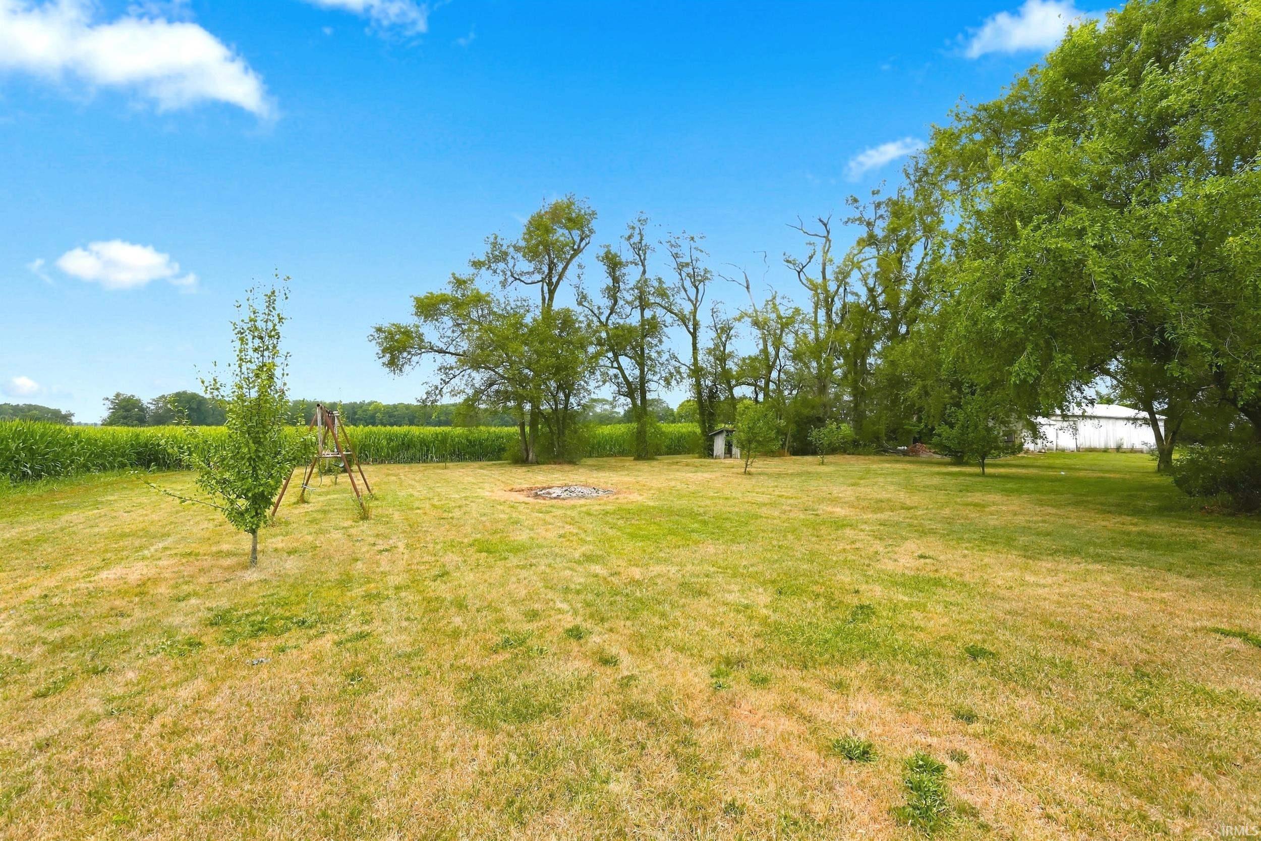 Expansive lawn area featuring mature trees, a small shed, and a fire pit