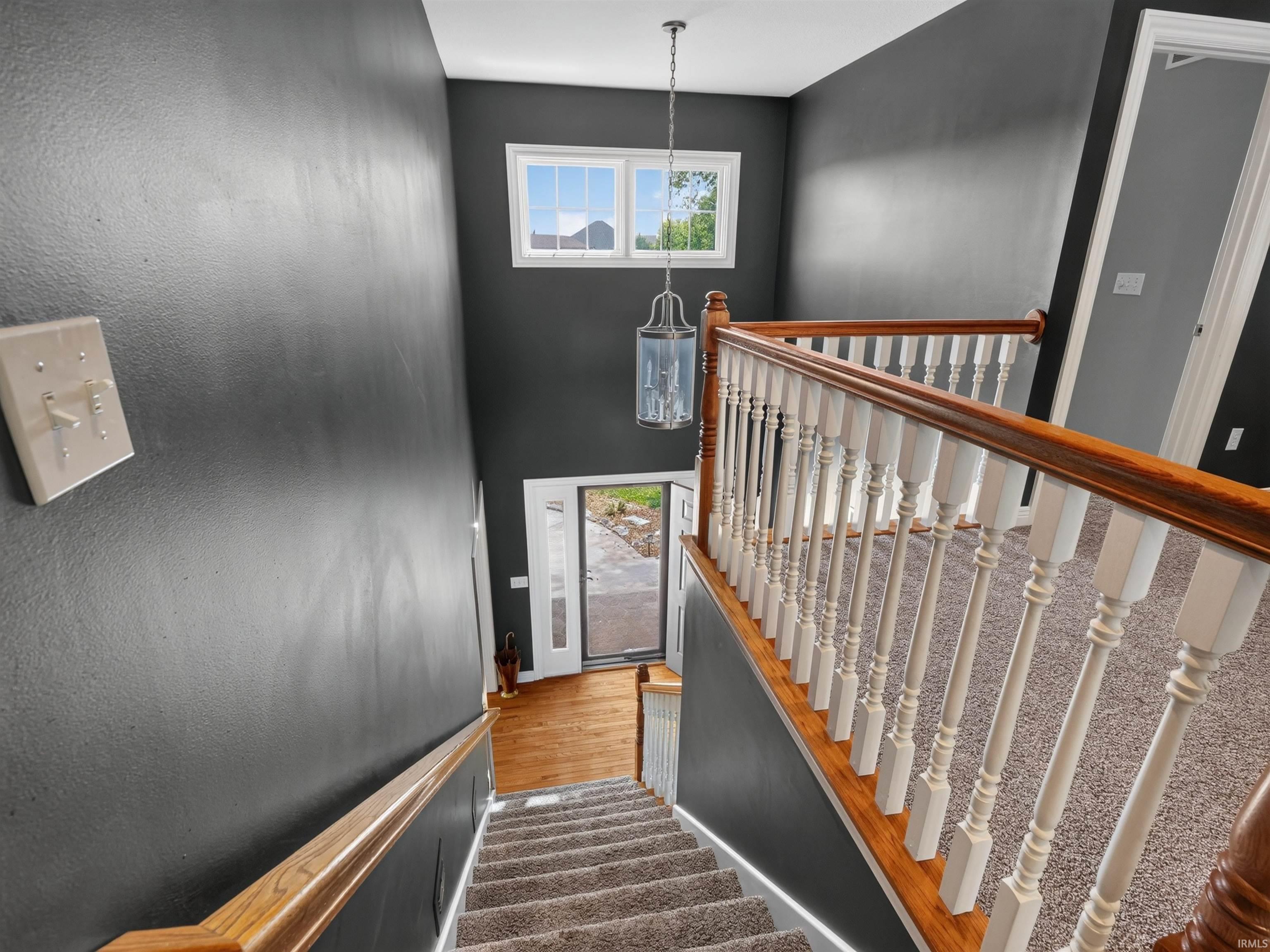 Two-story entryway with a decorative chandelier, upper-level window, wood-finish handrail, and carpeted stairs