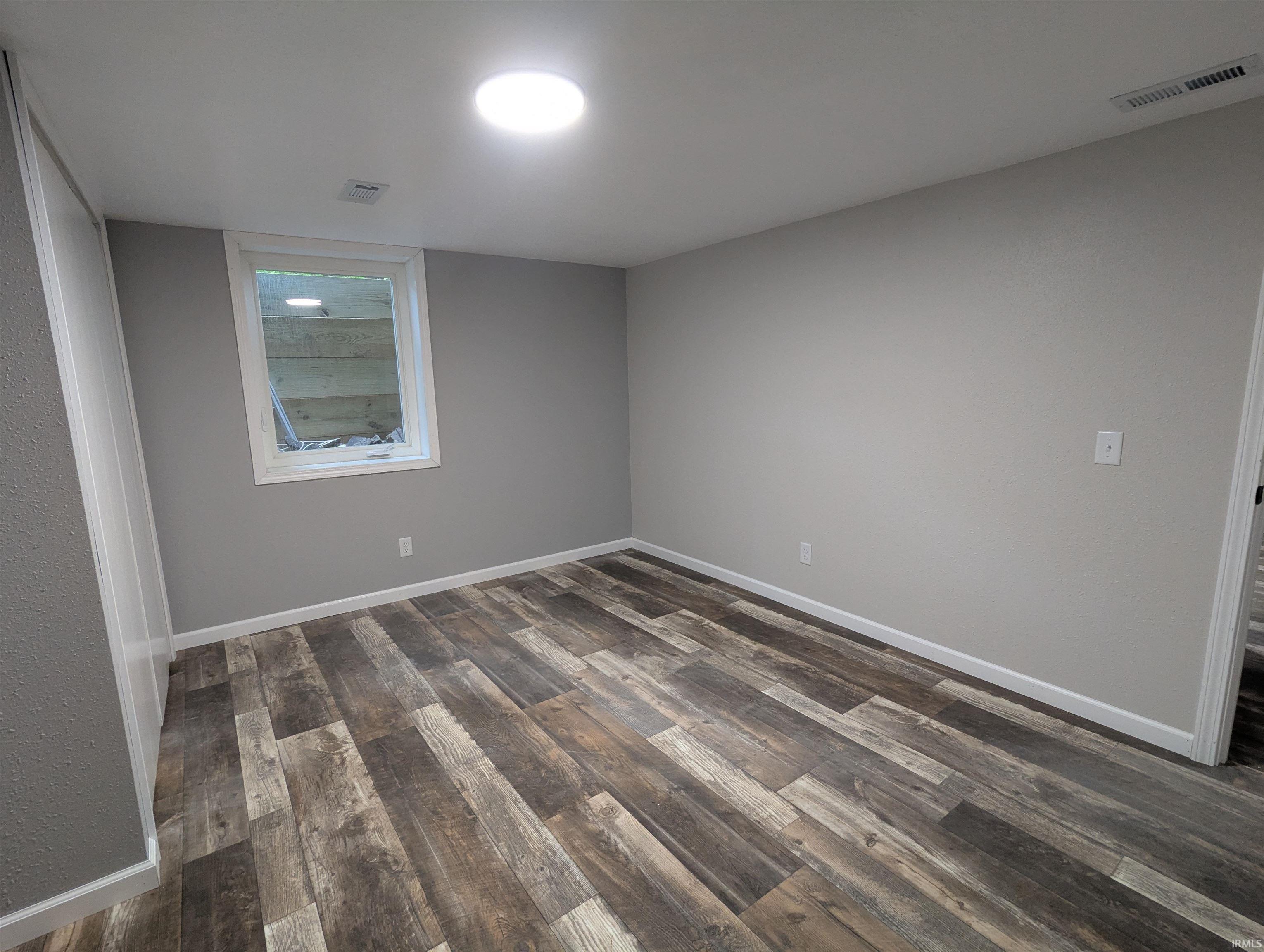 Spacious interior room featuring wood-finish flooring, light gray wall paint, and white trim