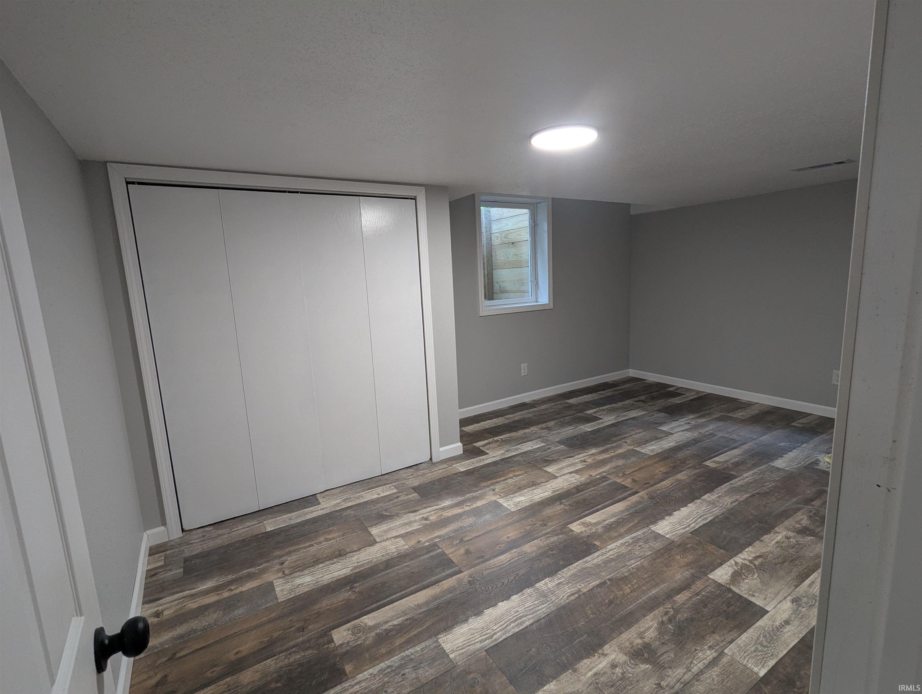 Spacious room featuring wood-finish flooring, light gray walls, white trim, and a white bi-fold closet