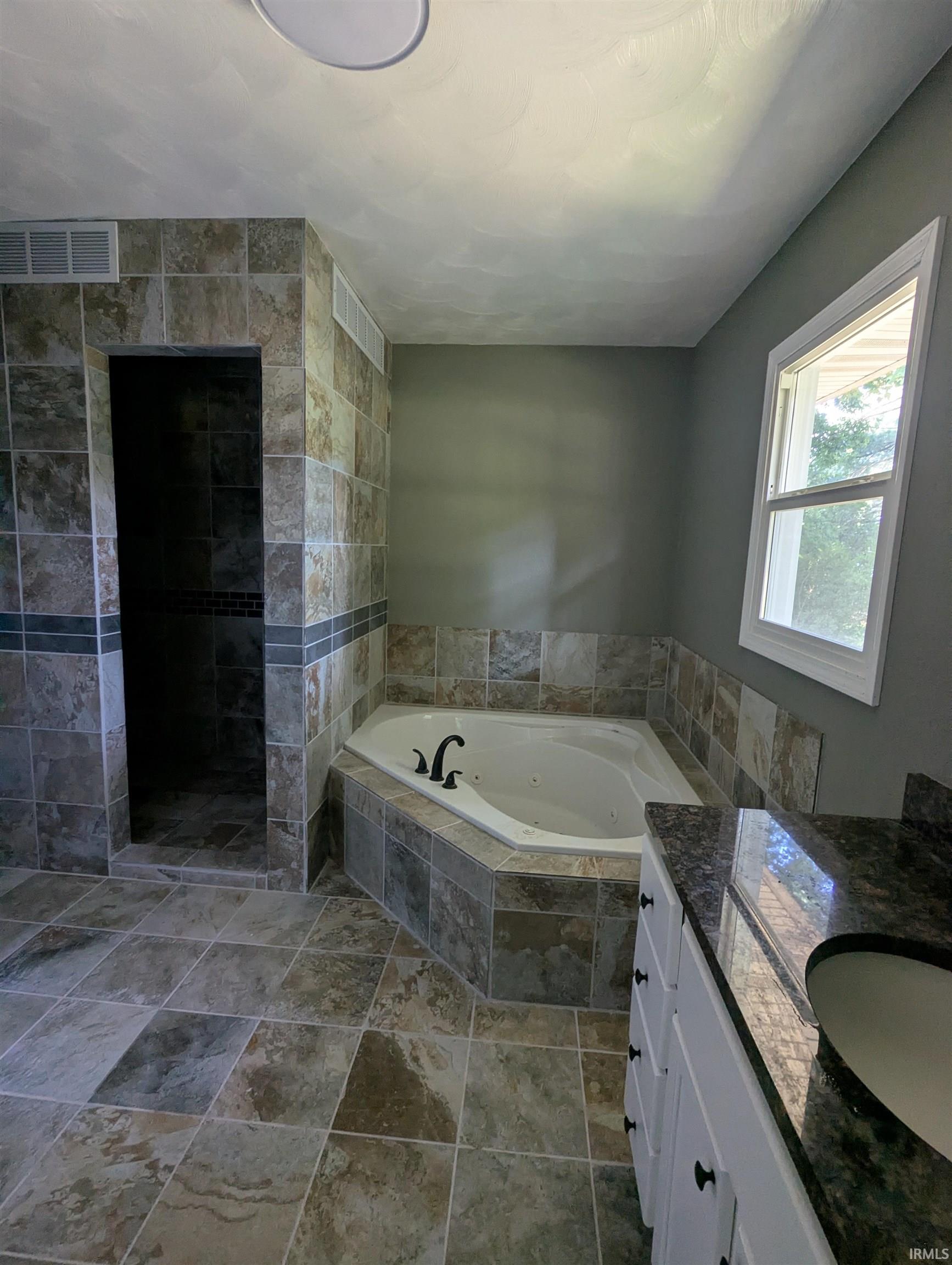 Tiled bathroom featuring a corner soaking tub and walk-in shower