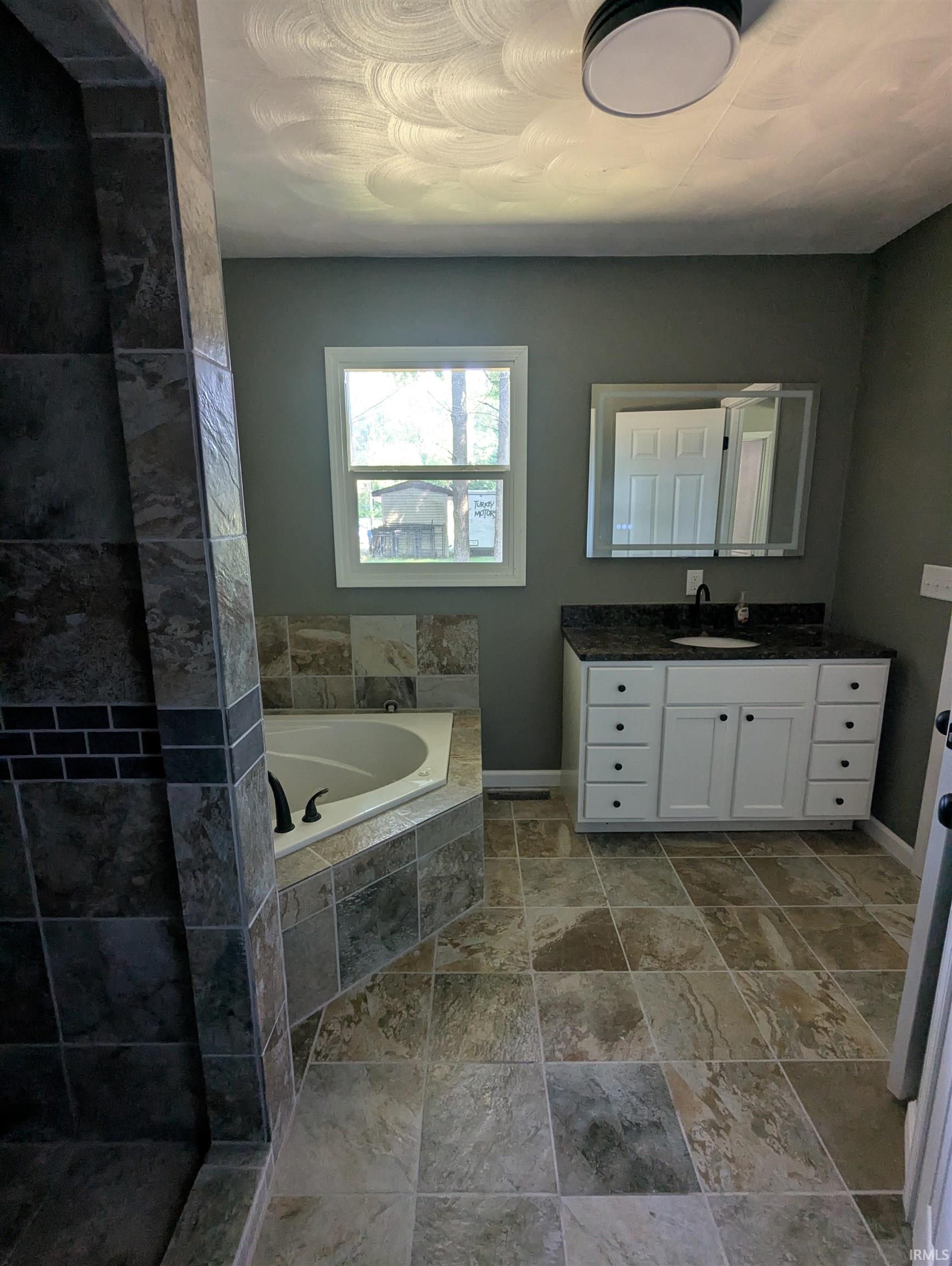 Bathroom featuring a corner soaking tub with tile surround, a separate tiled shower, and multi-toned floor tiling