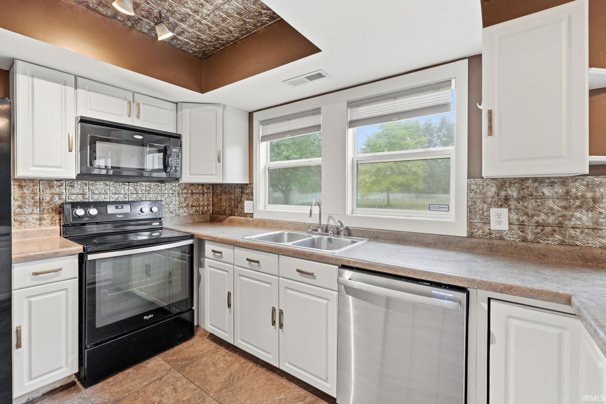White cabinetry, stainless steel dishwasher, dual basin sink, black electric range, and an integrated microwave