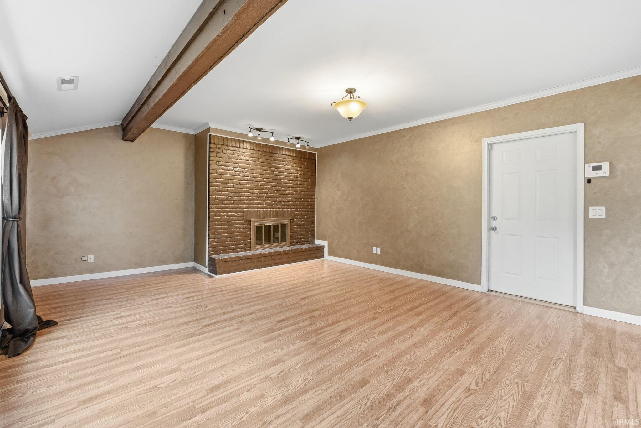 Brick fireplace with a metal insert, wood-finish flooring, exposed ceiling beam, crown molding, and a paneled entry door