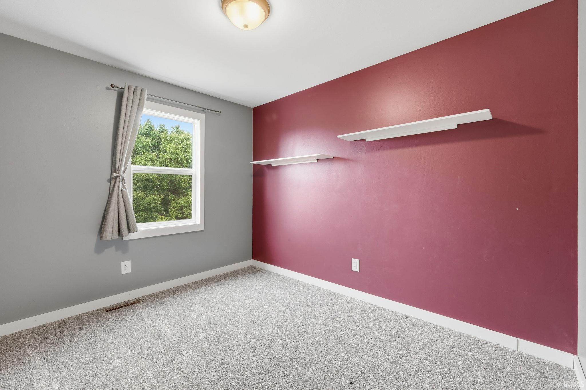 White trim, gray walls, maroon accent wall, wall-mounted shelving, and light-colored carpeting