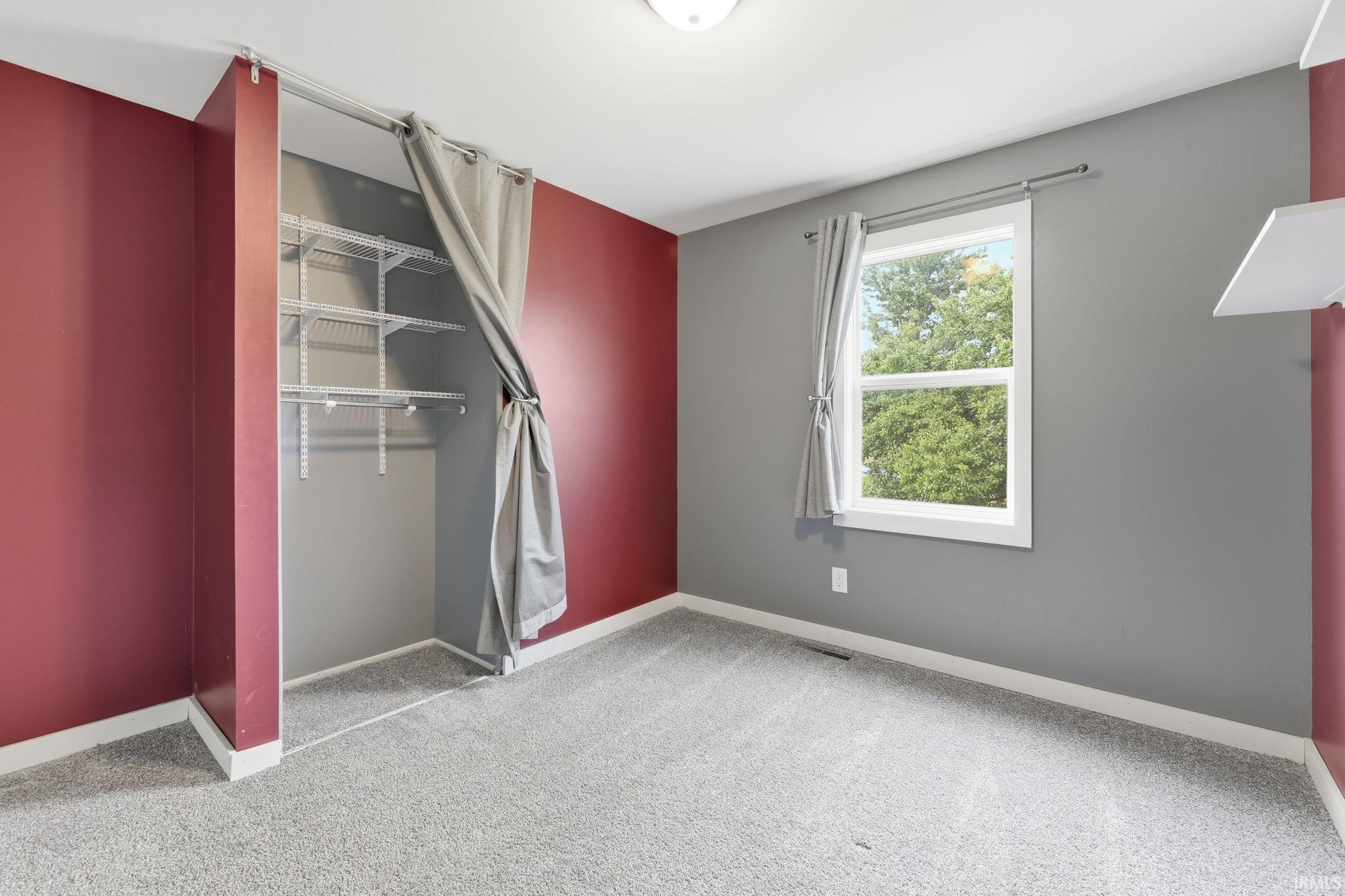 Wall-to-wall carpeting, built-in wire shelving, and a single window with white trim