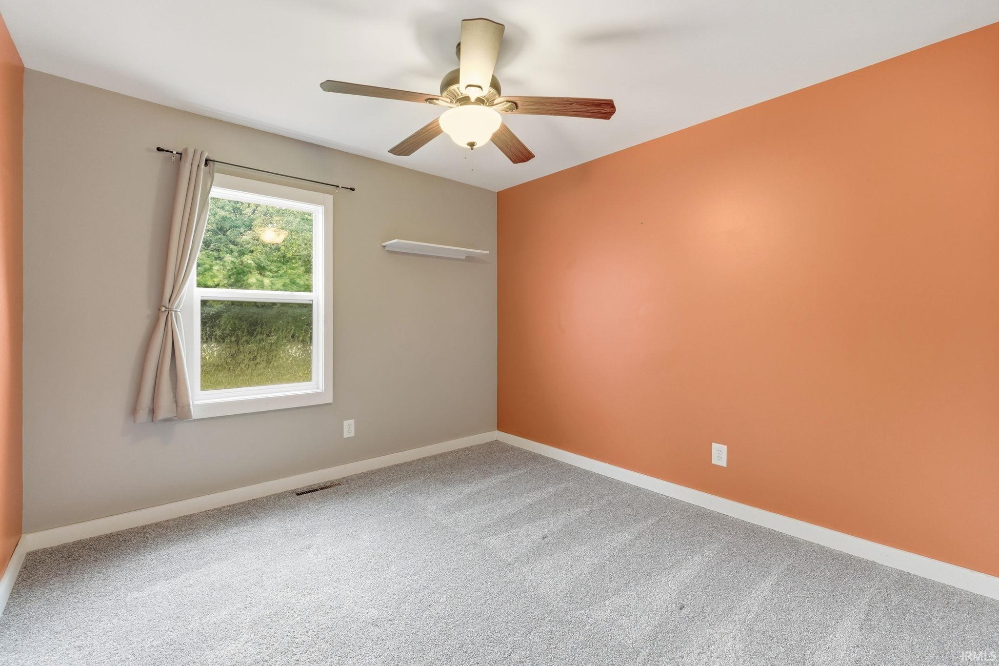 Neutral tone walls with an accent wall, window with white trim, wood-finish ceiling fan with integrated lighting, and light-toned carpet