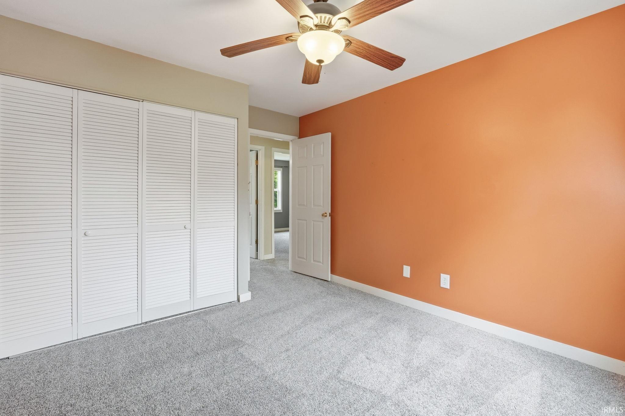 Ceiling fan with wooden blades, wall-to-wall carpeting, louvered bi-fold closet doors, and painted walls