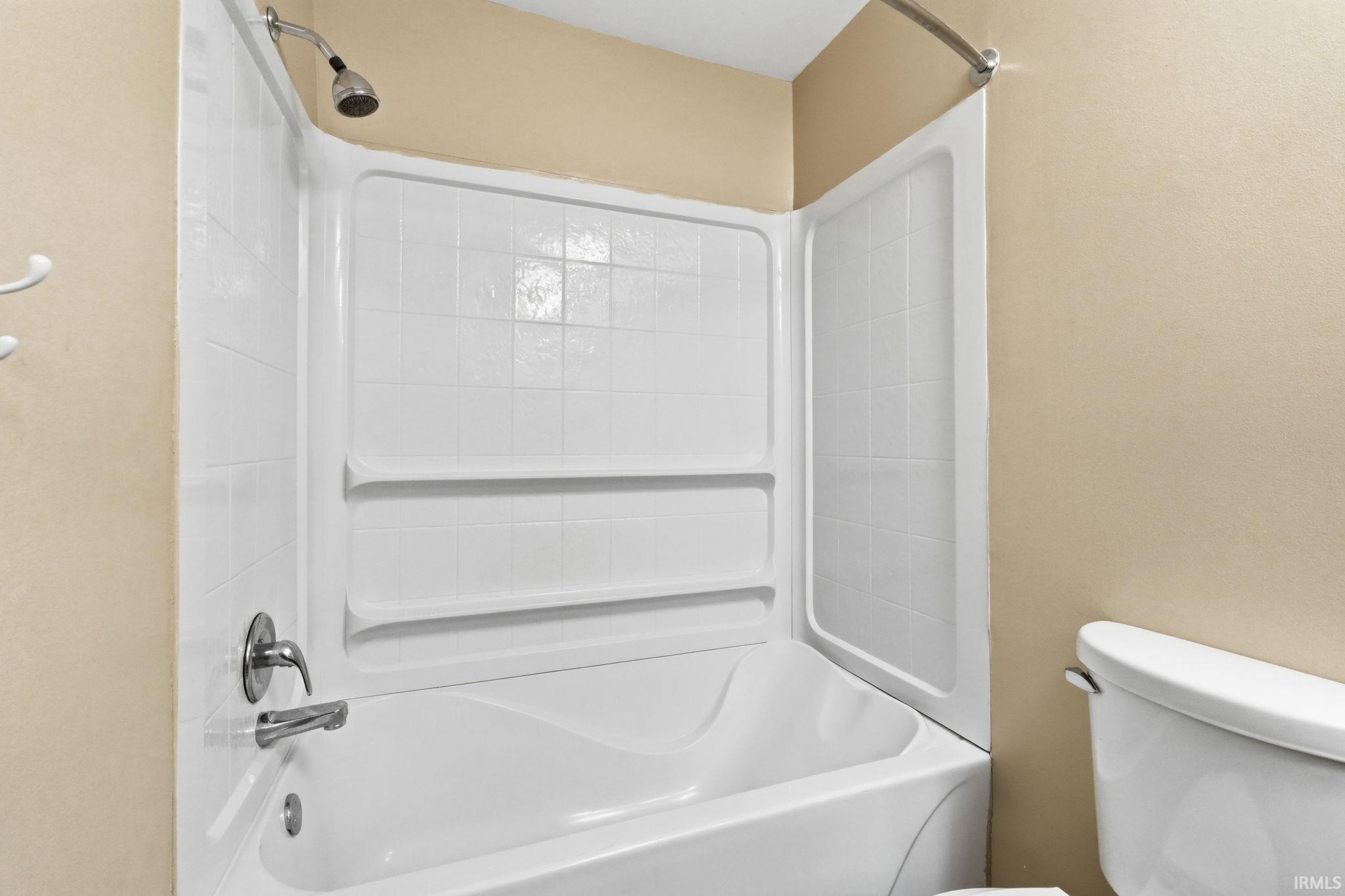 White bathtub with an integrated shower, chrome fixtures, and a white shower surround