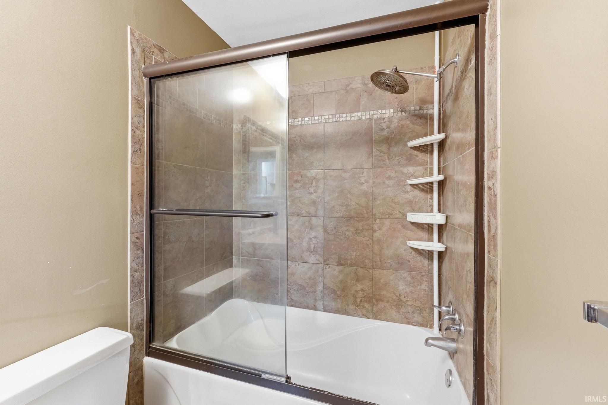 Bathtub shower combination with sliding glass doors, tiled surround, and a rain shower head