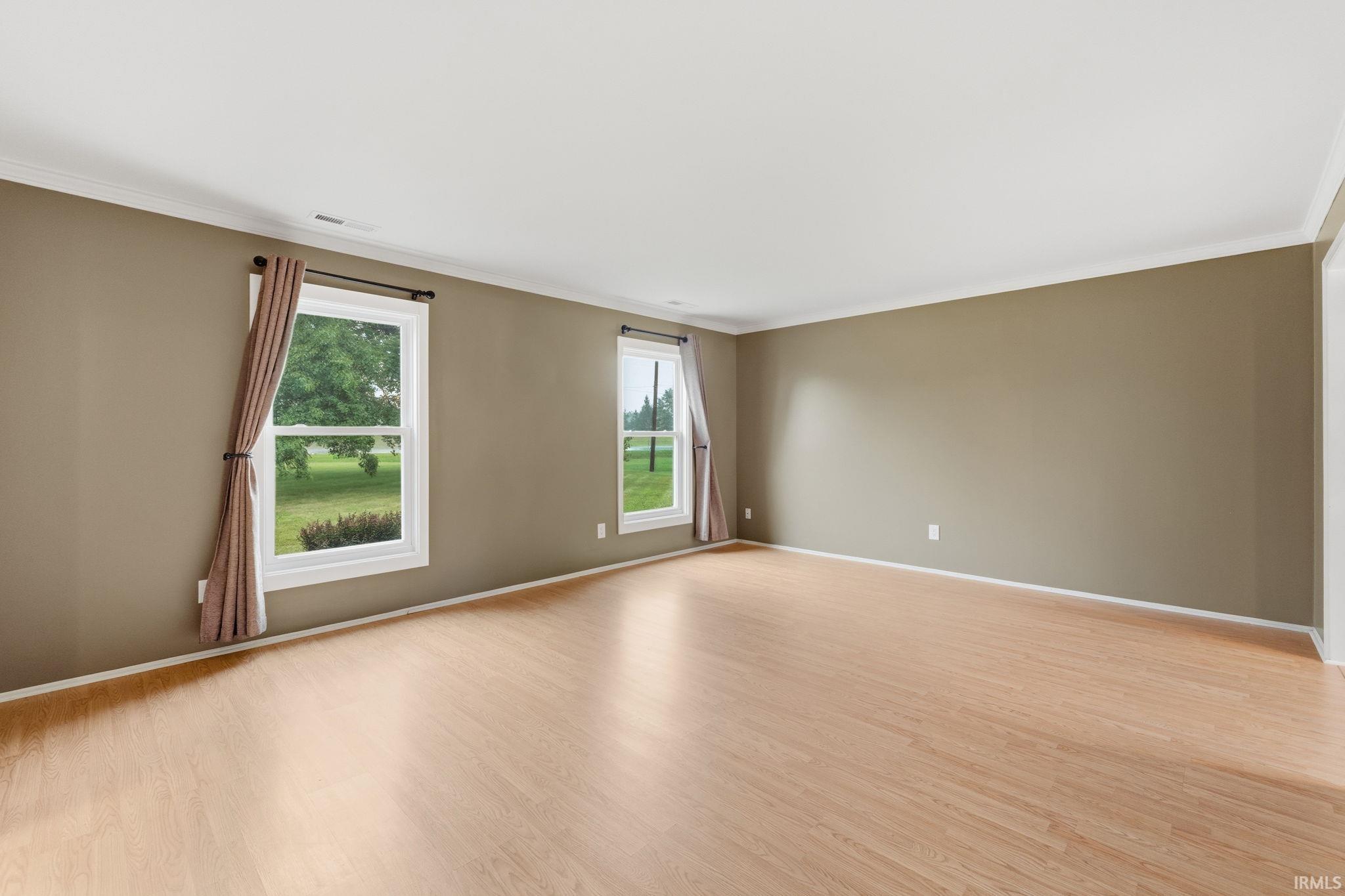 Spacious room featuring wood-finish flooring, two windows with white trim, and crown molding