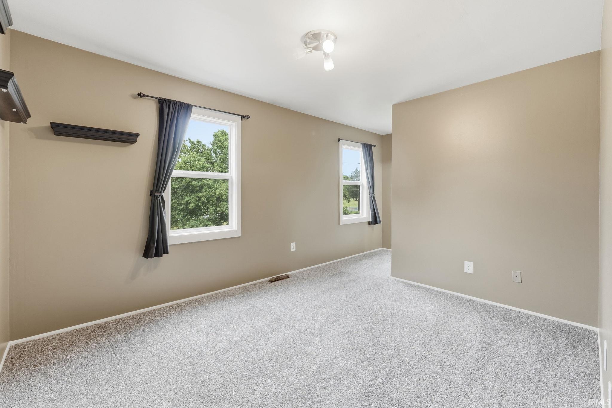 Neutral tone walls, light gray carpeting, two windows, and a ceiling-mounted light fixture