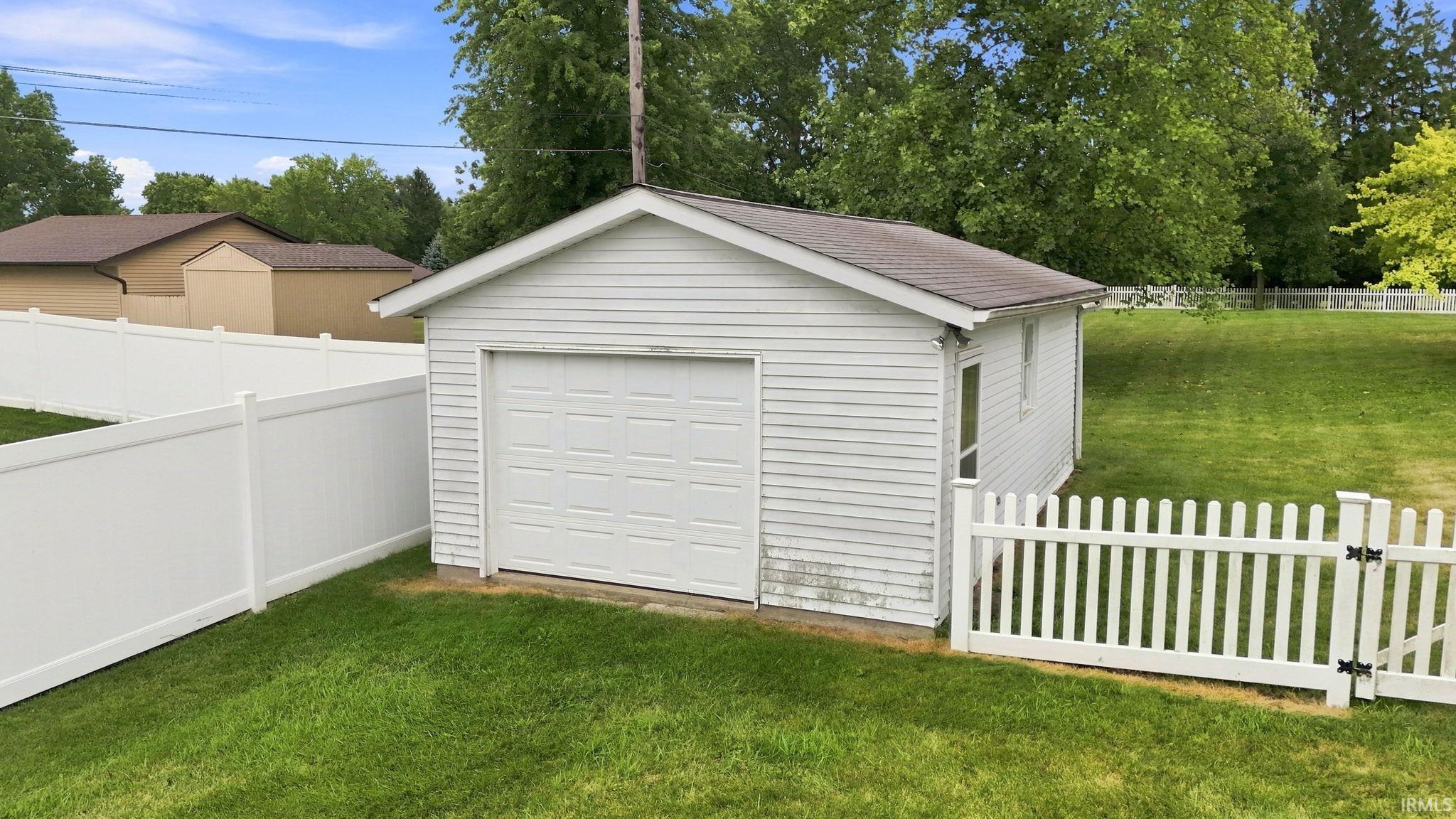 Detached garage with white siding and a white garage door, featuring a white picket fence and a white privacy fence