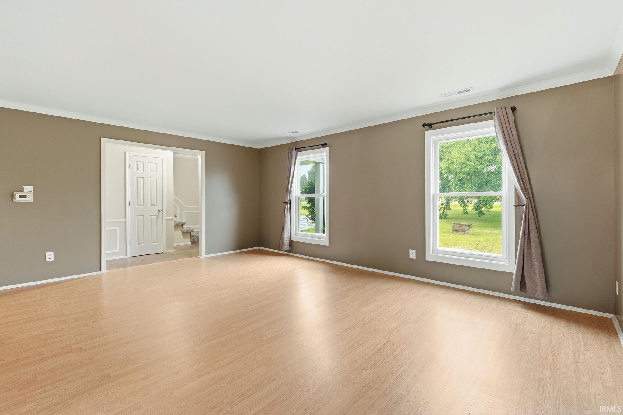Wood-finish flooring, two large windows, white crown molding, and a paneled door