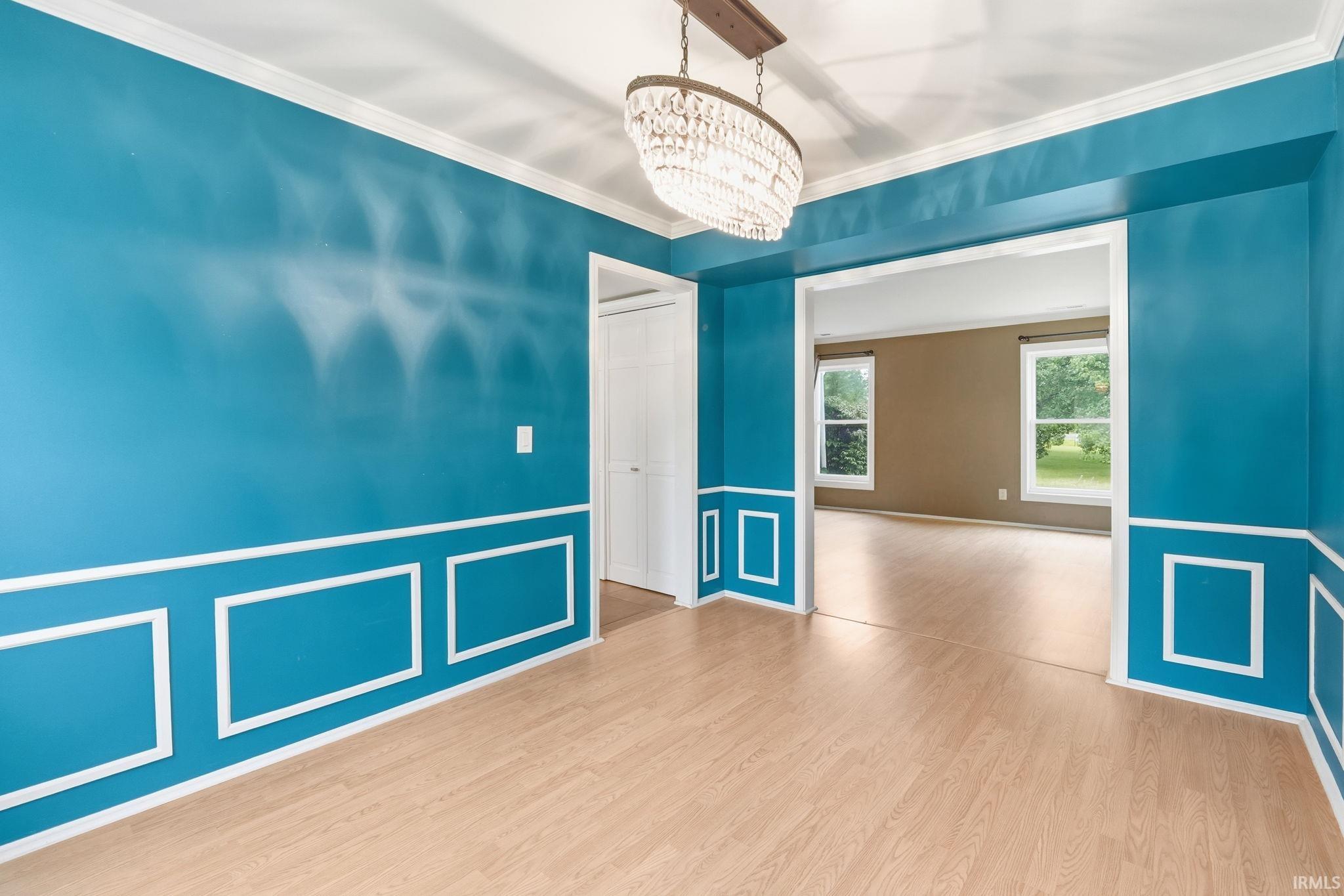 Recessed panel accent wall, wood-finish flooring, and a crystal chandelier