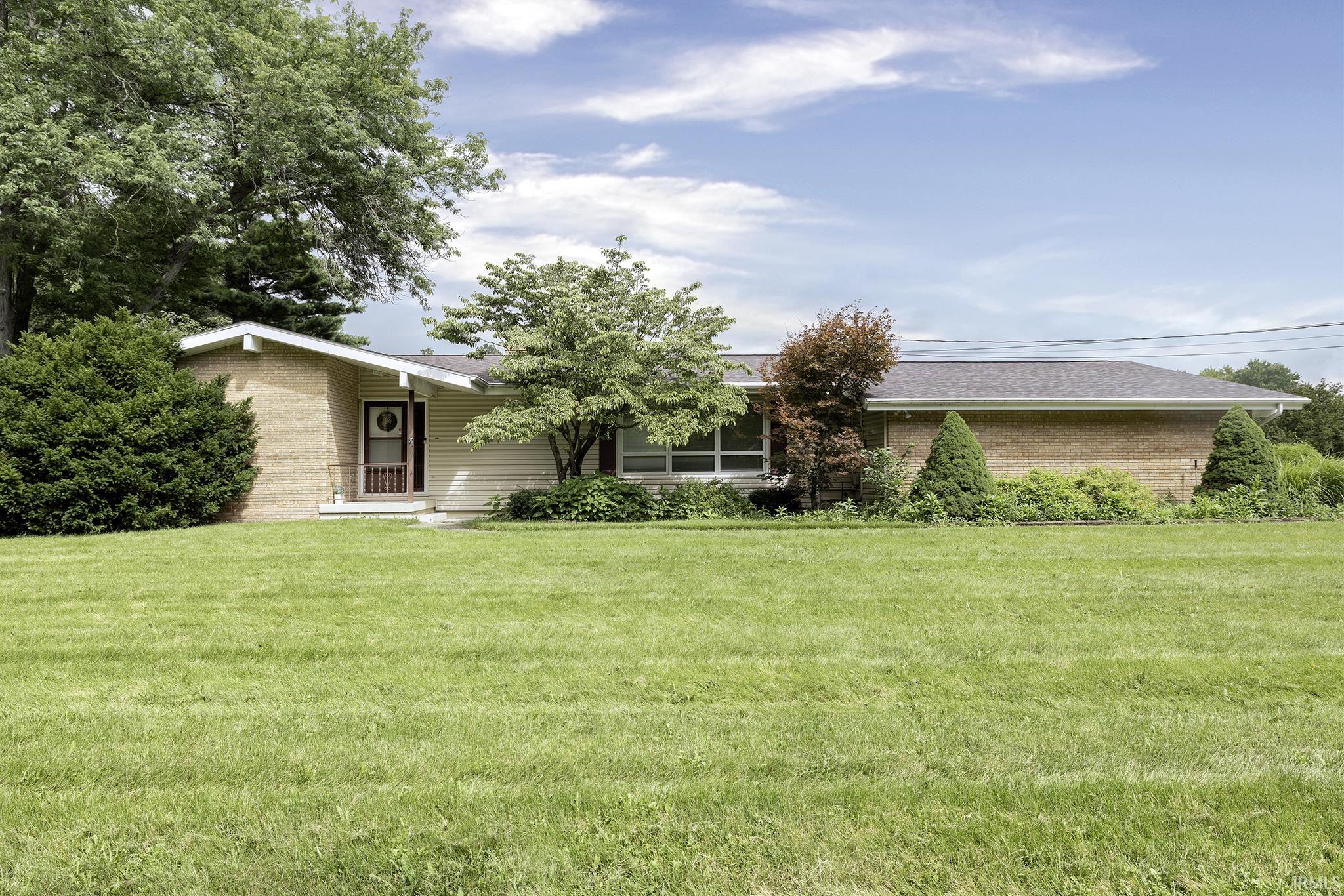 Expansive front lawn with mature landscaping, brick and siding exterior, and a covered entry