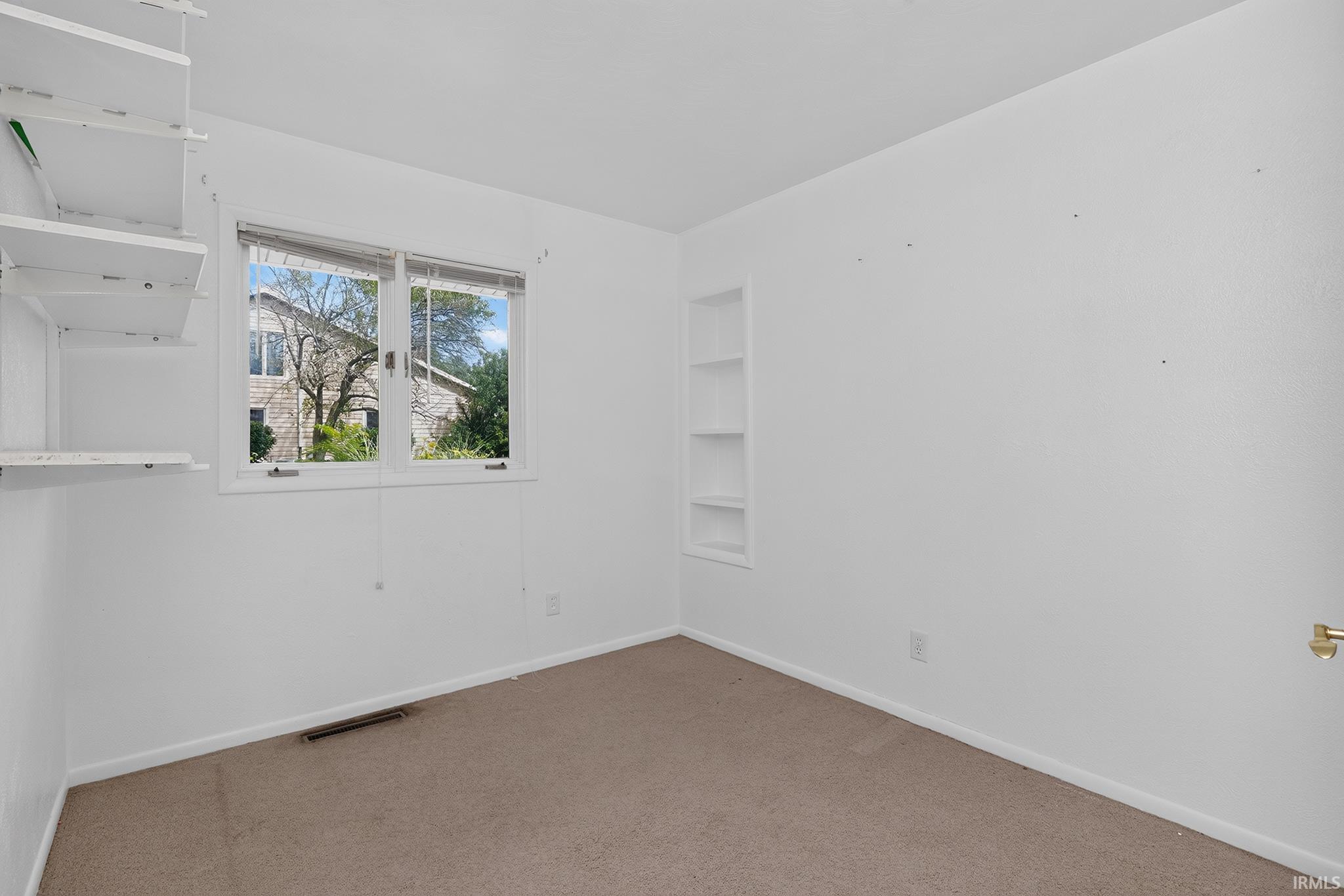 White walls with built-in shelving, a double window, and carpeted flooring