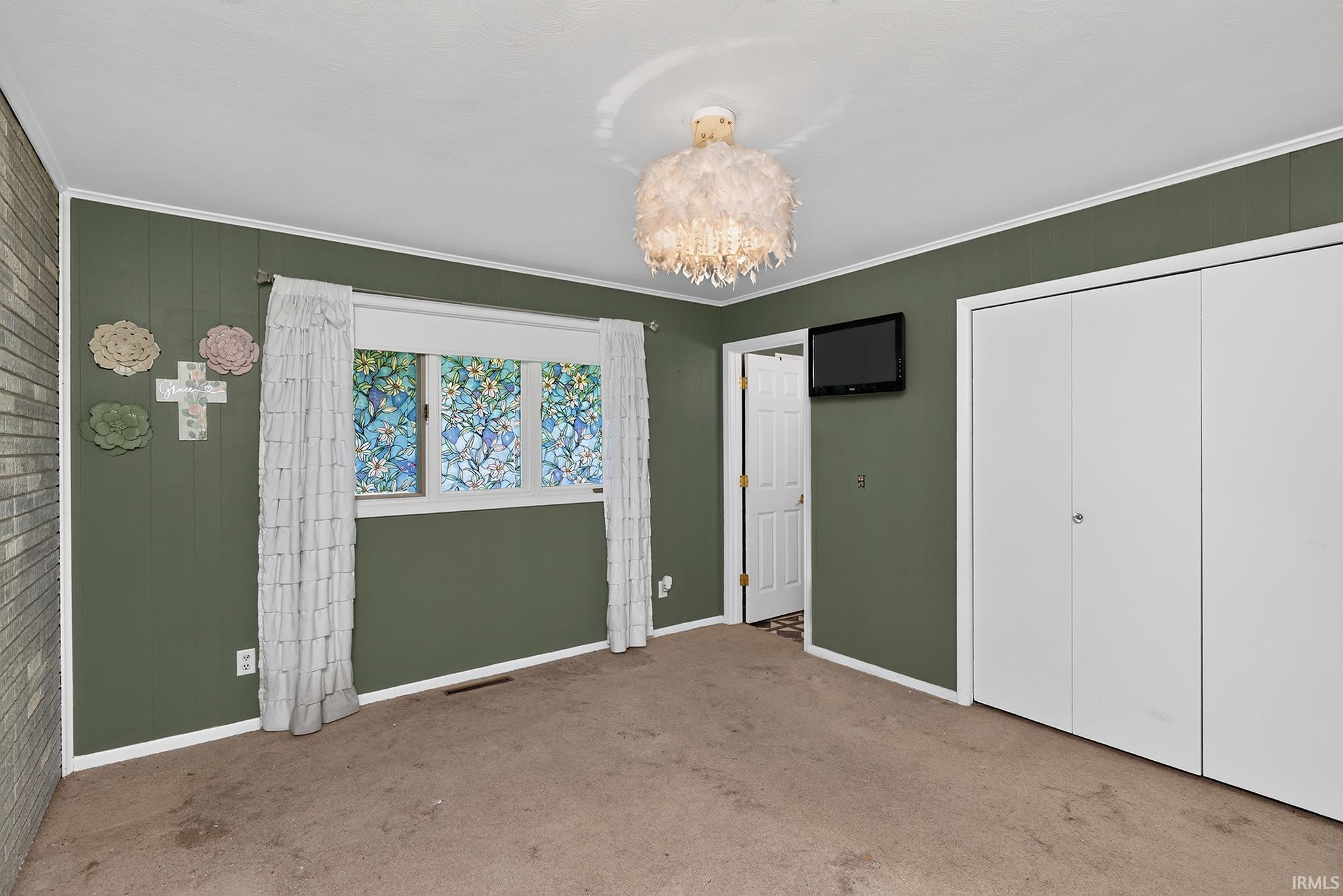 Built-in closet with bi-fold doors, textured wall paneling, window with decorative film, and overhead light fixture