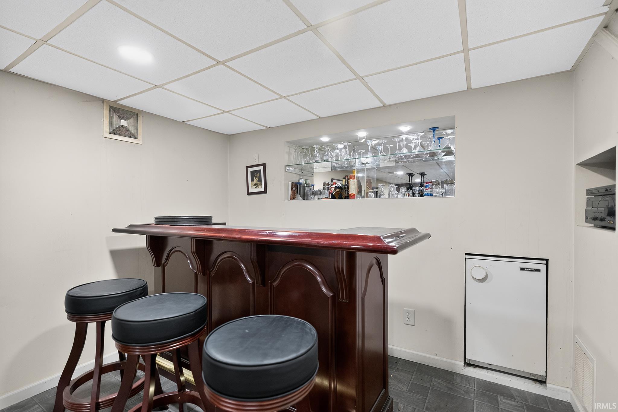 Built-in bar with dark wood-finish cabinetry, black countertop, and integrated shelving with recessed lighting
